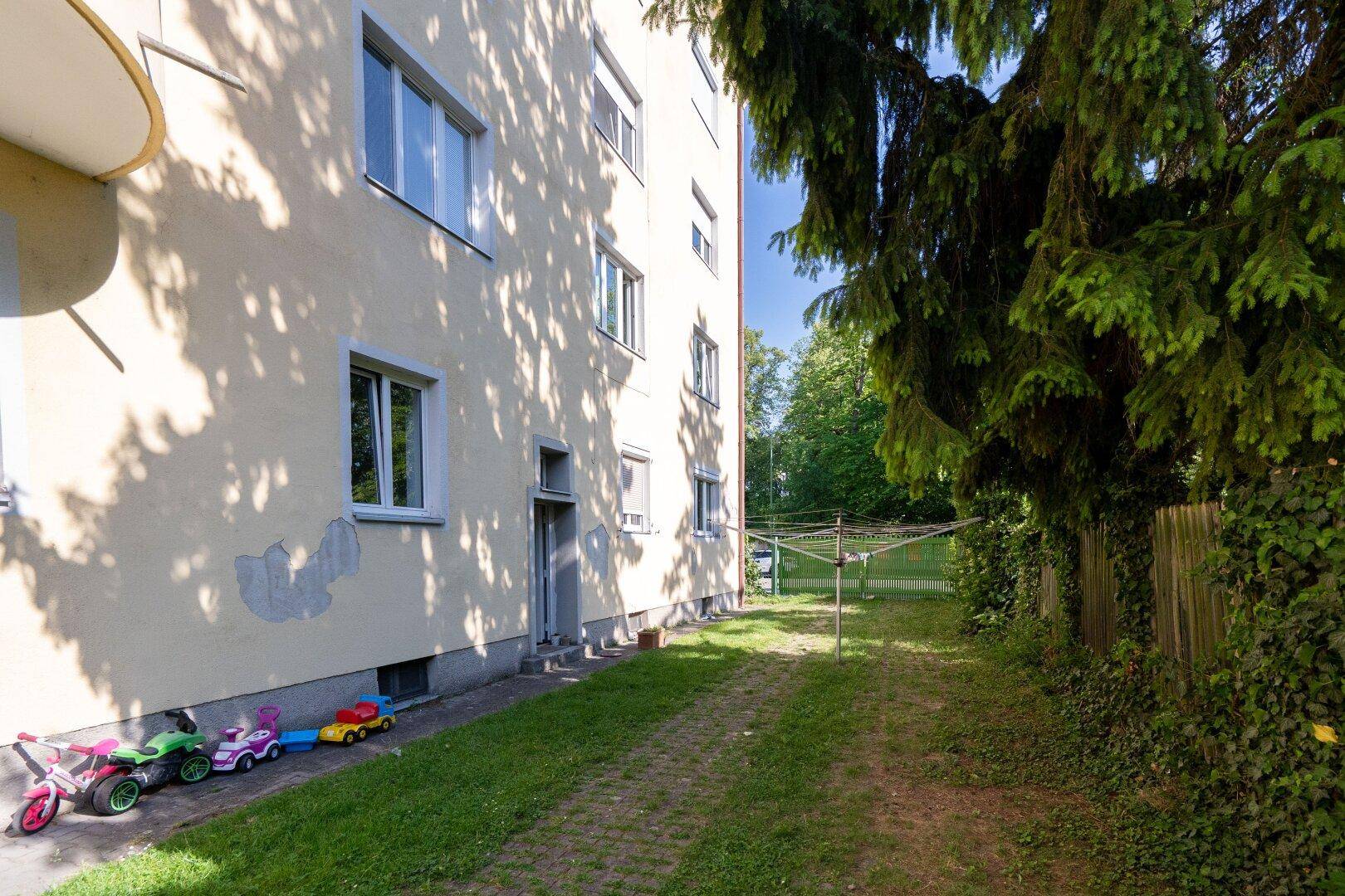 Seitenansicht eines Wohngebäudes mit Rasenfläche und Spielzeug im Vordergrund.