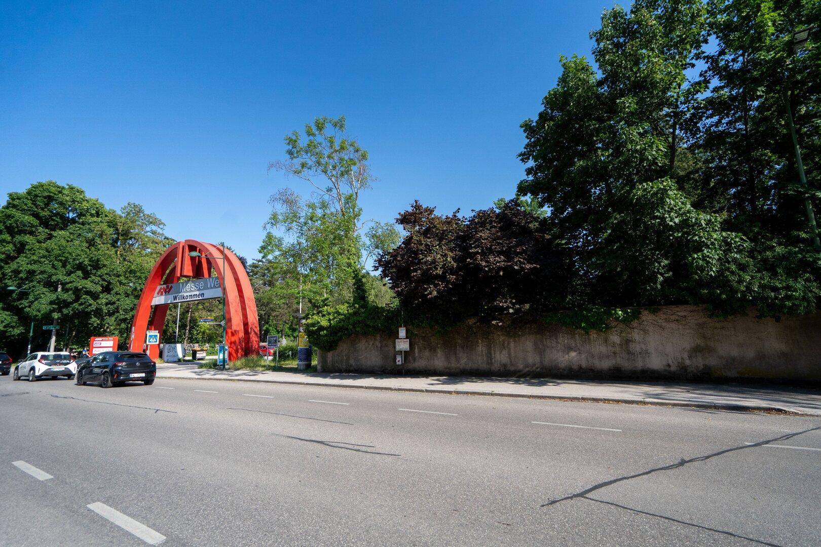 Weitläufige Straßenansicht mit viel Grün, Gebäuden und einem auffälligen roten Torbogen.