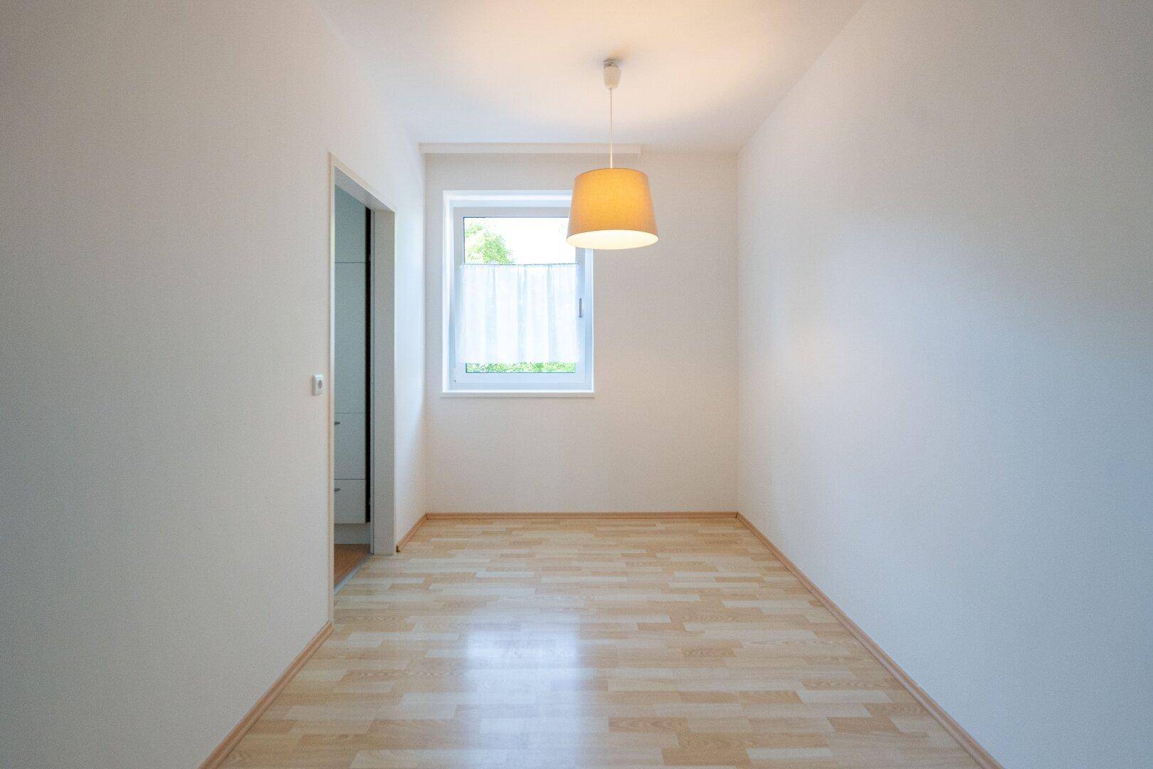 Helles Zimmer mit hellem Laminatboden und einem Fenster, ideal als Schlaf- oder Arbeitszimmer.