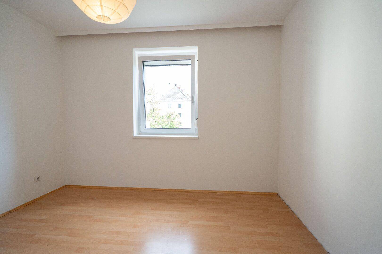 Helles Zimmer mit Laminatboden und einem Fenster, das einen Blick nach draußen bietet.