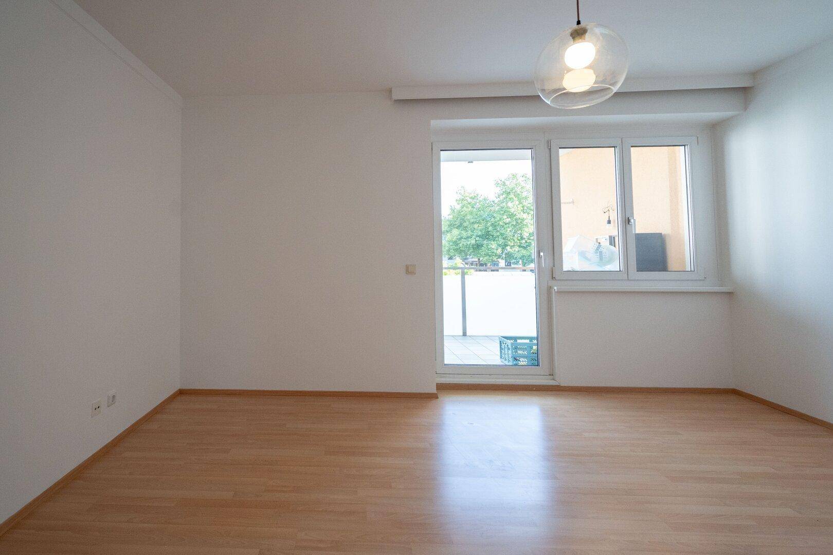 Geräumiges Wohnzimmer mit Laminatboden und Zugang zu einem sonnigen Außenbereich.