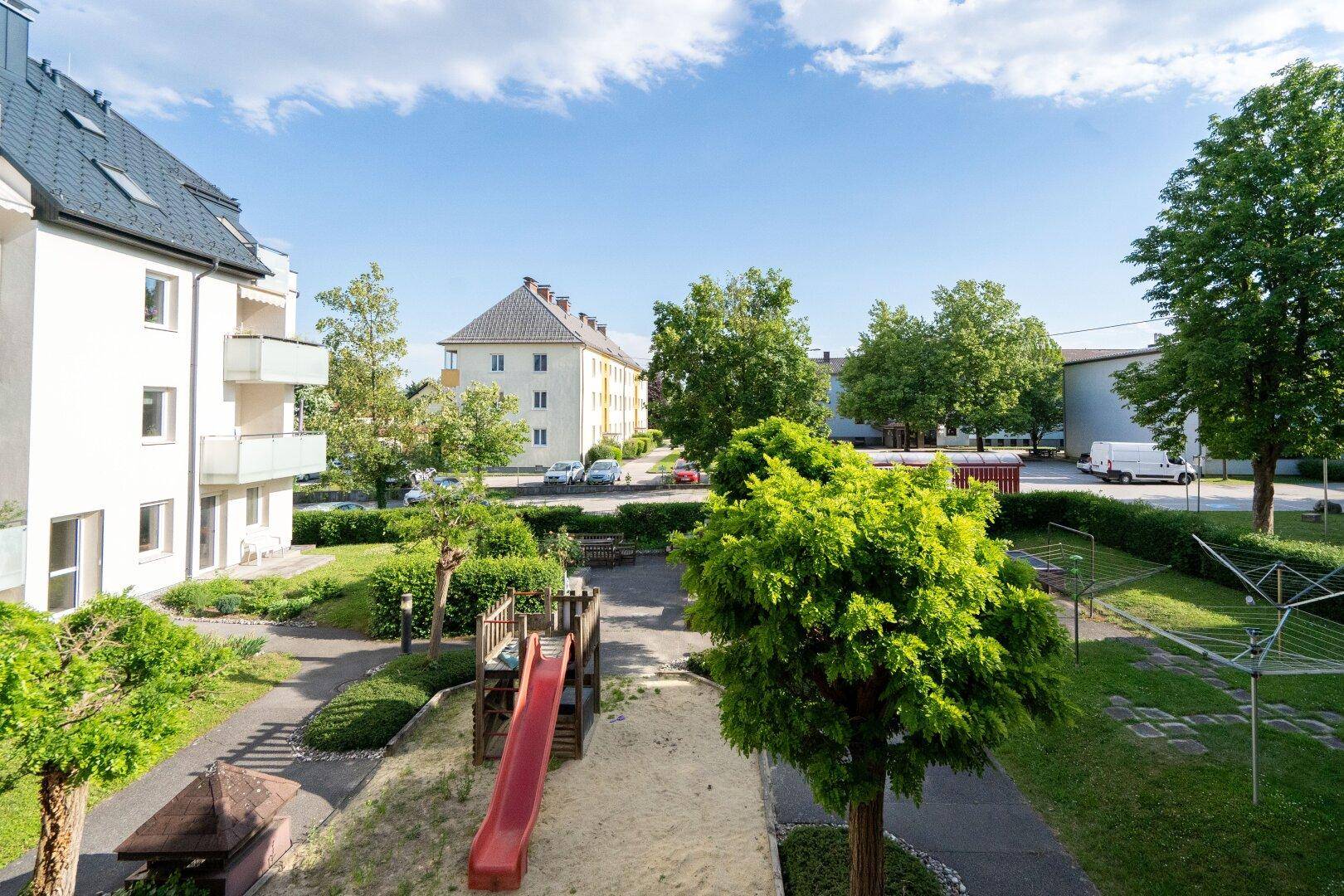 Grüner Innenhof mit Kinderspielplatz, Rutsche und Sandkasten, umgeben von Wohngebäuden.