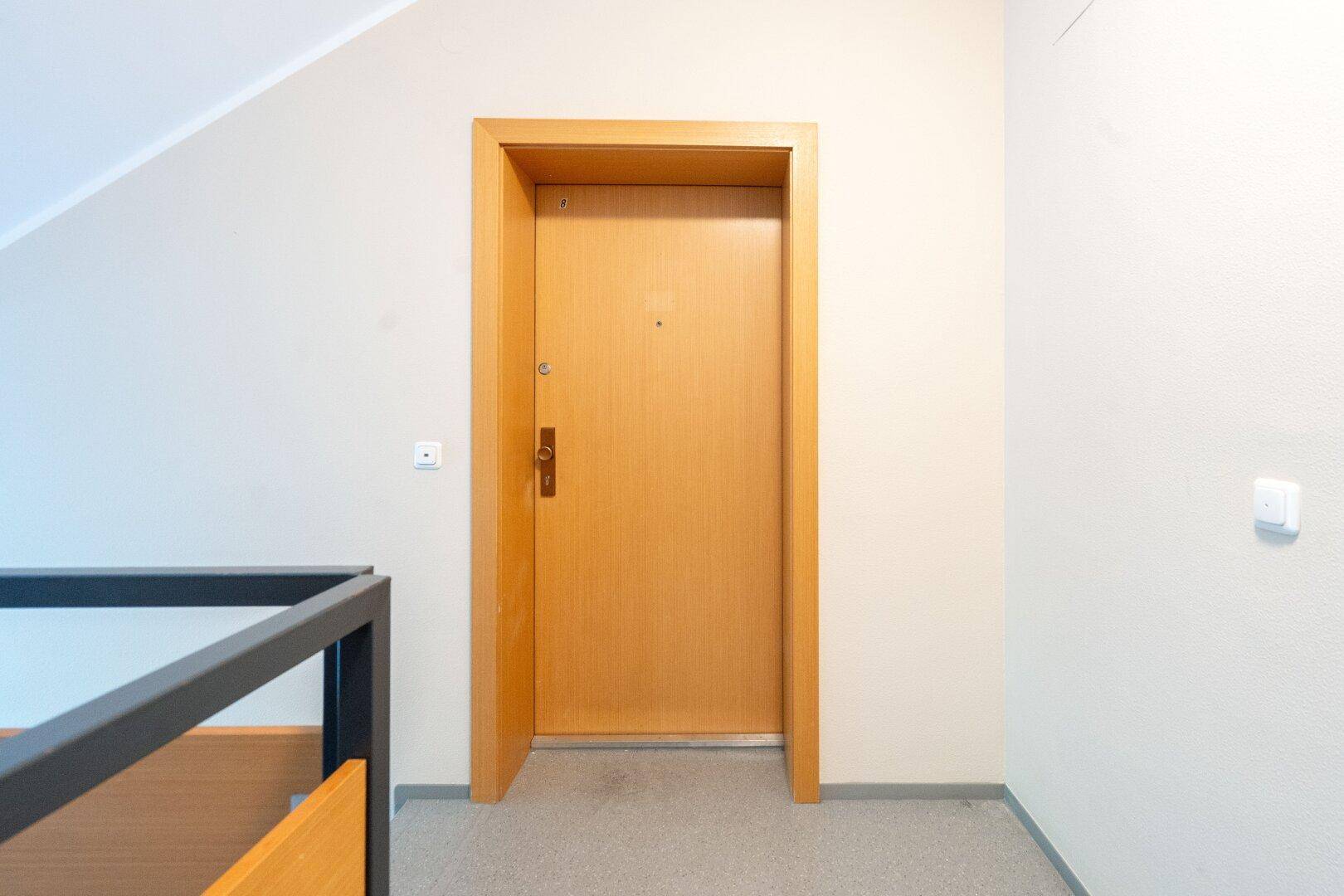 Eingangsbereich der Wohnung mit einer stabilen Holztür und hellem Teppichboden.