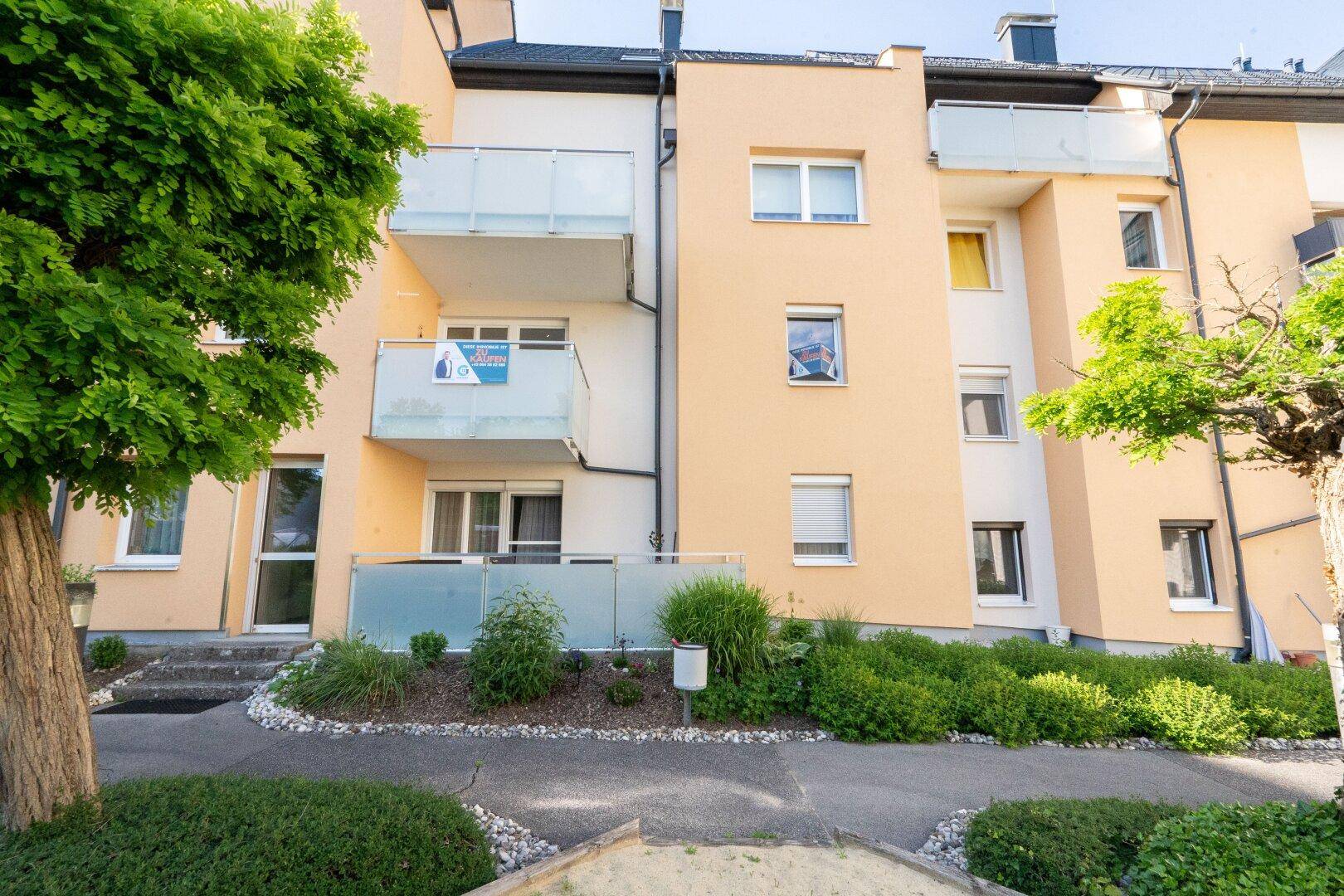 Fassade eines Mehrfamilienhauses mit Balkonen und einer kleinen Grünfläche im Erdgeschoss.