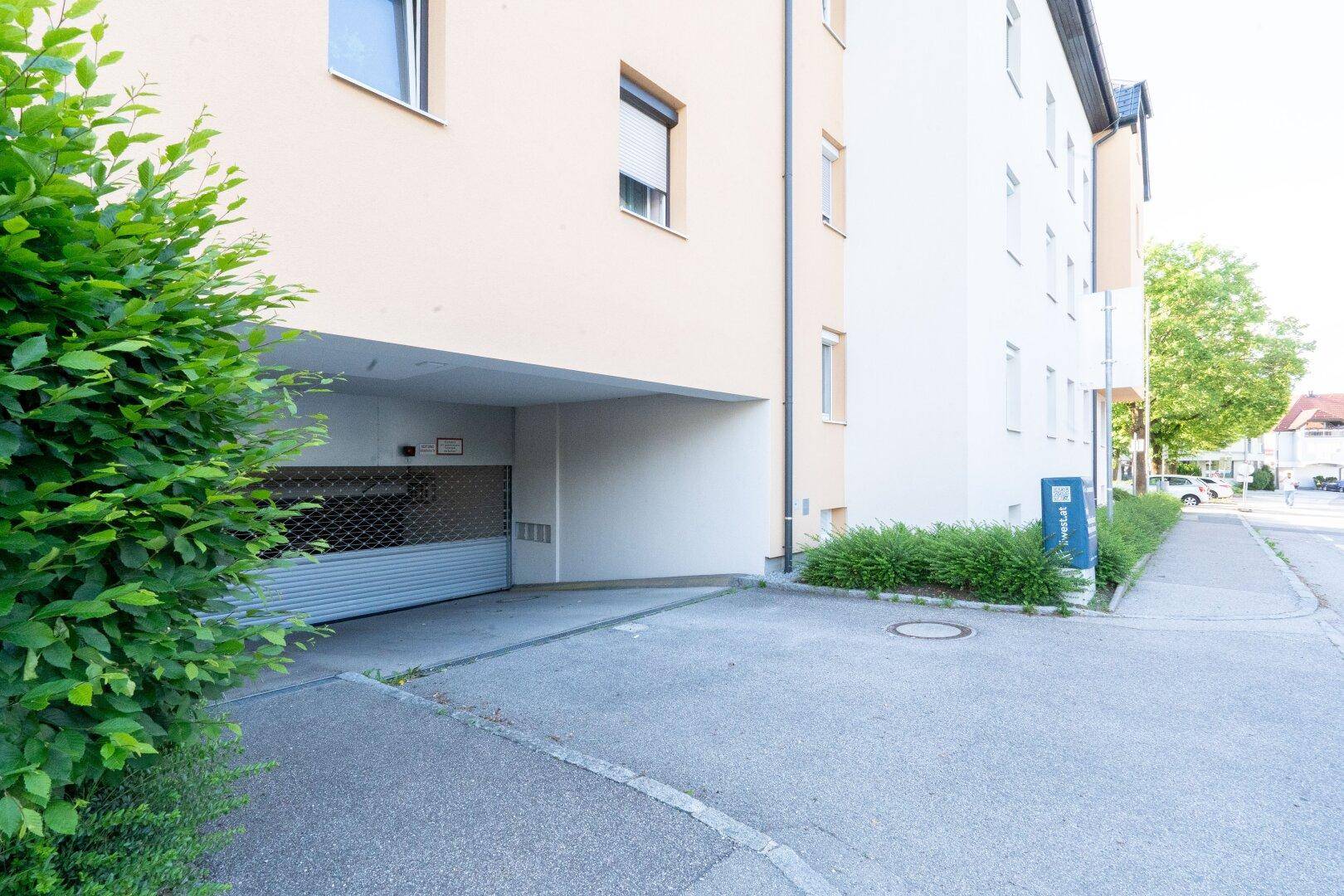 Einfahrt zur Tiefgarage eines Wohngebäudes von der Straße aus, umgeben von Grünflächen.