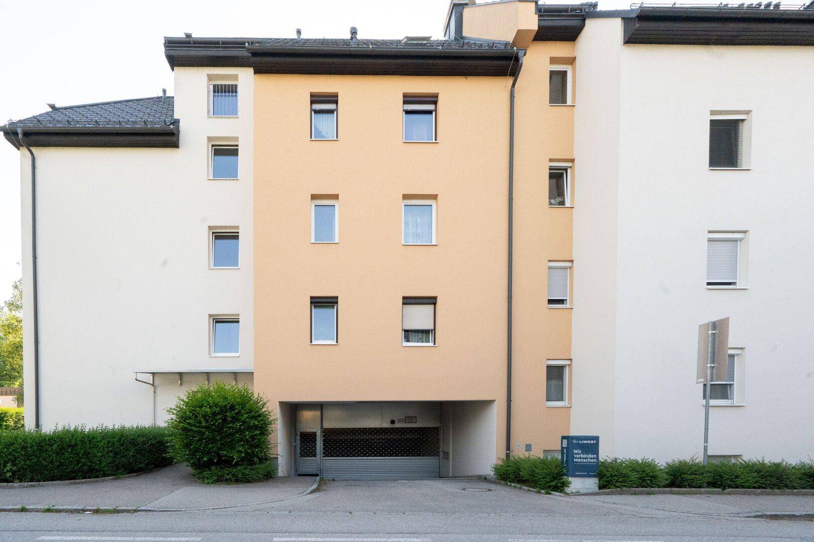 Ansicht der Gebäudefassade mit integrierter Tiefgarageneinfahrt und mehreren Fenstern.