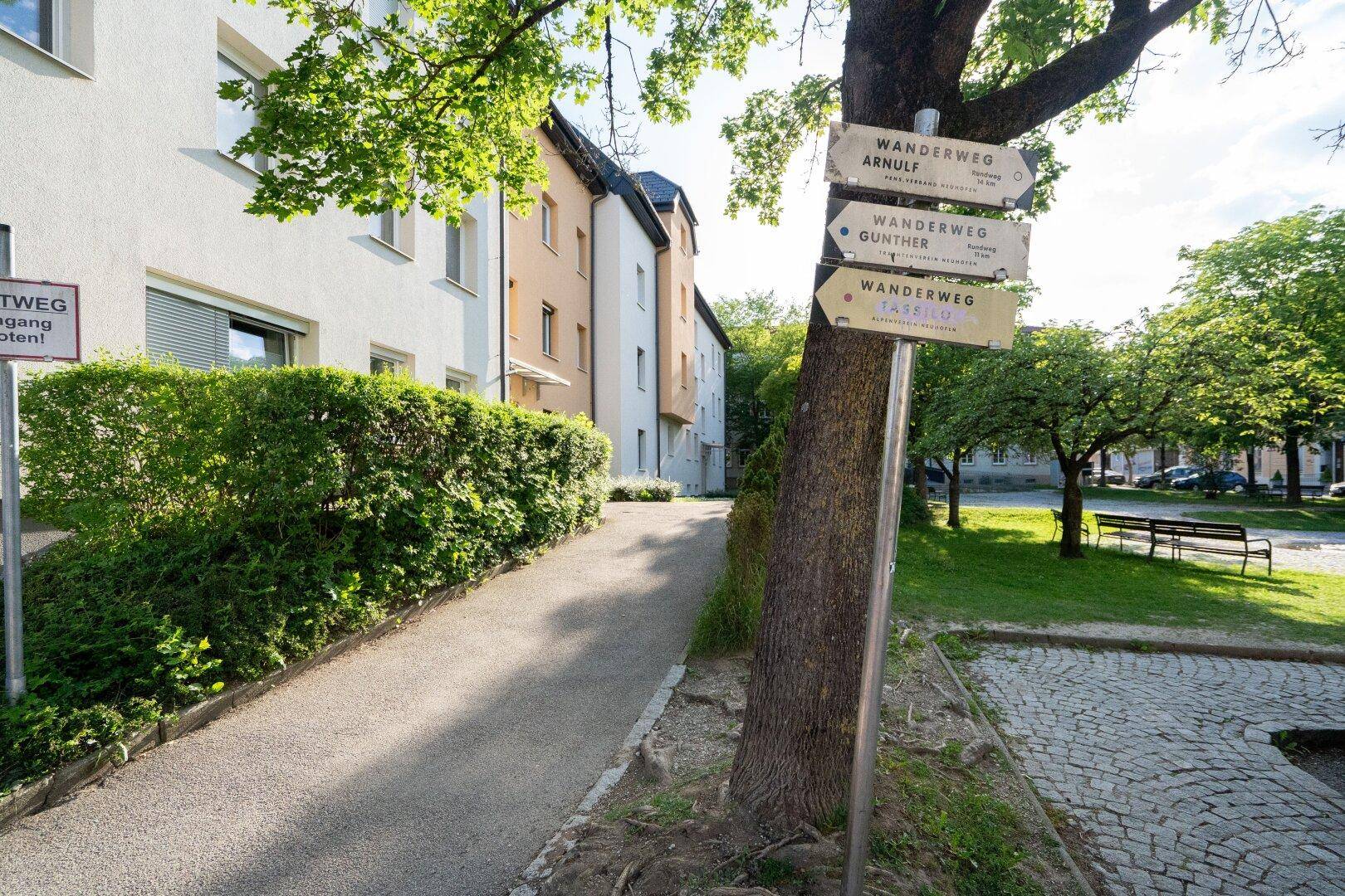 Außenbereich mit einem Wanderwegweiser und einem gepflegten Grünstreifen neben den Gebäuden.