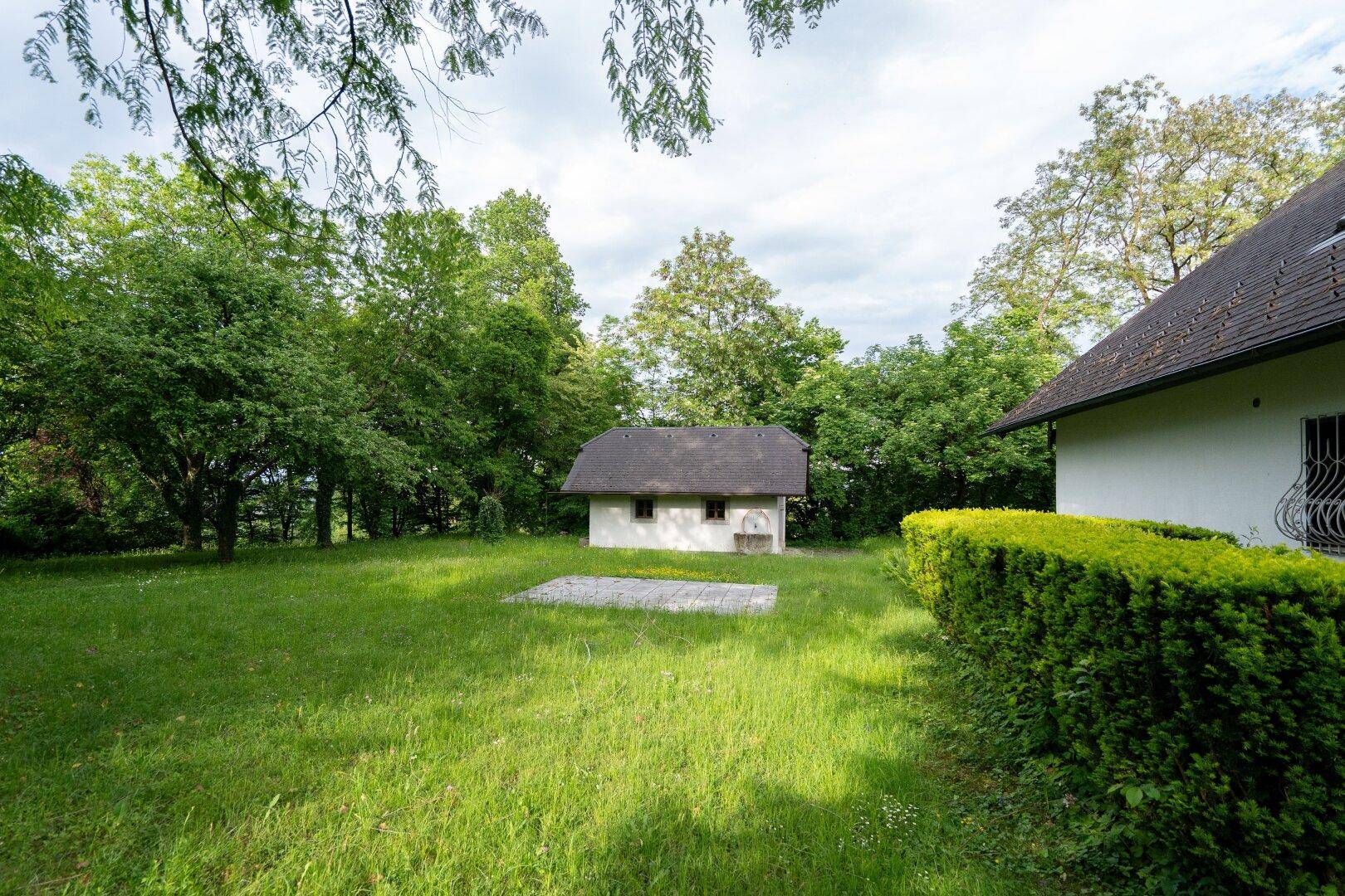 Weitläufiger Gartenbereich mit einem kleinen Nebengebäude und dem Haupthaus im Hintergrund.