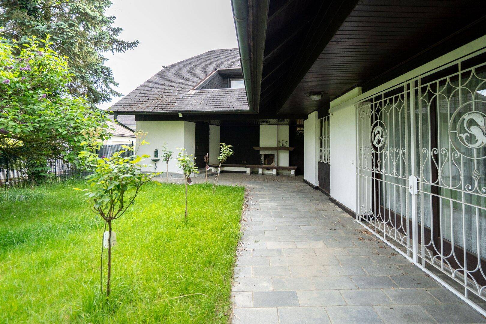 Gepflasterte Terrasse entlang des Hauses mit einem Außenkamin und Blick ins Grüne.