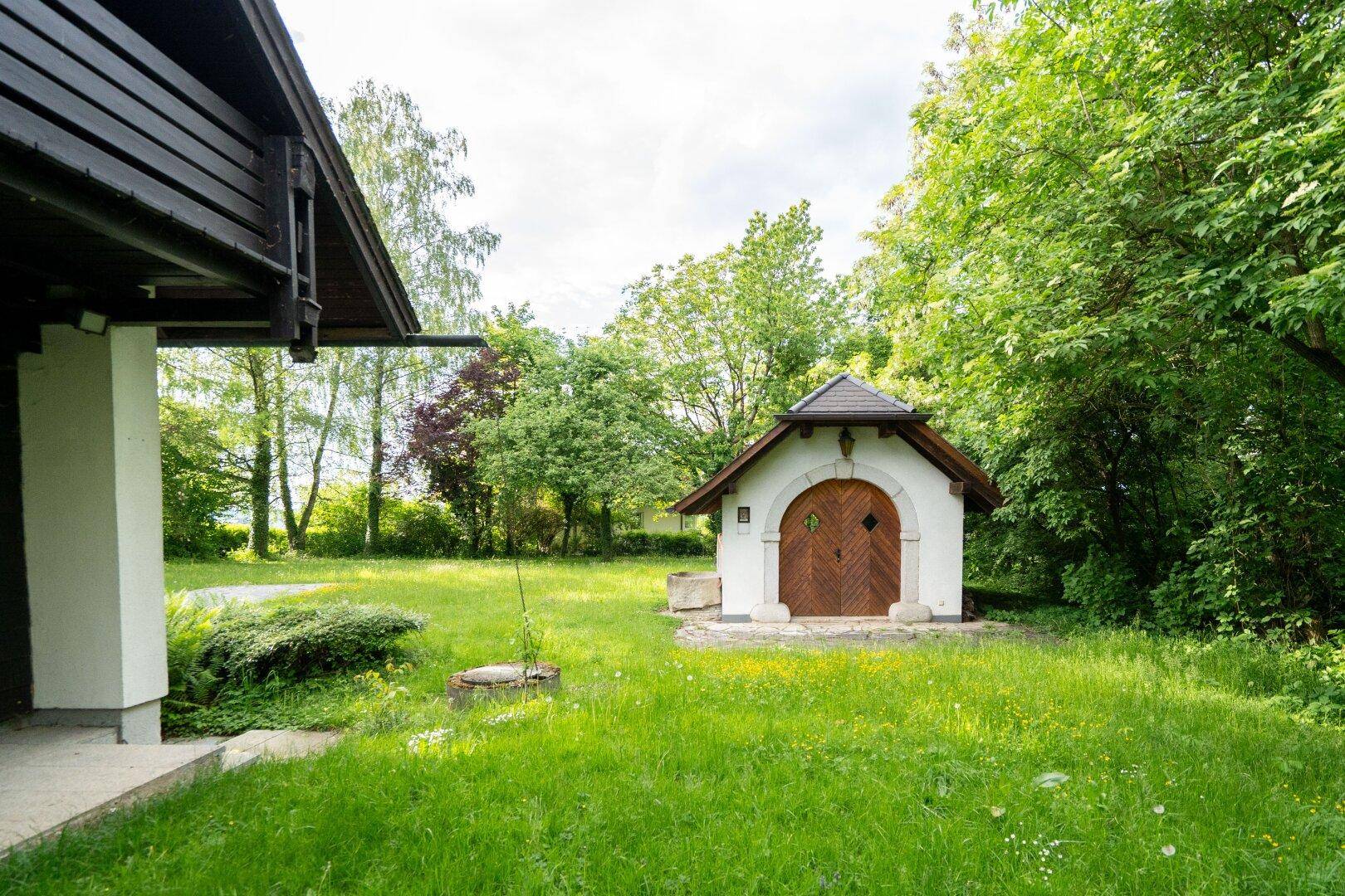 Malerisches kleines Gebäude mit Holztüren und Steinakzenten, umgeben von üppigem Grün.