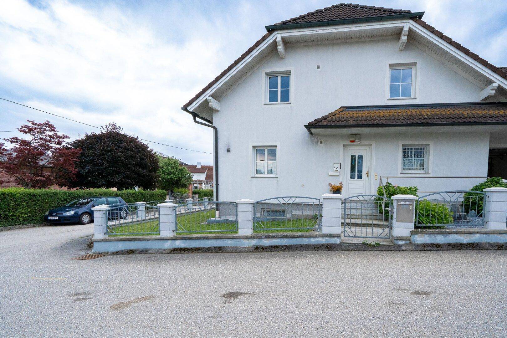 Eingangsbereich des Einfamilienhauses mit weißer Fassade und kleiner Gartenfläche.