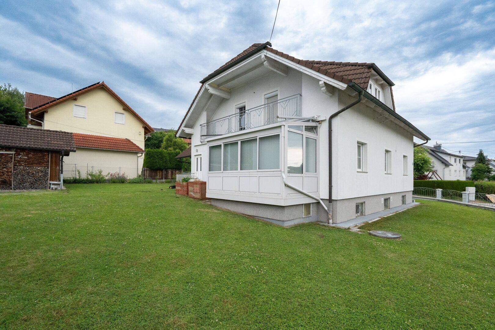 Rückseite des Hauses mit großem Rasenbereich und einem Wintergarten im Erdgeschoss.