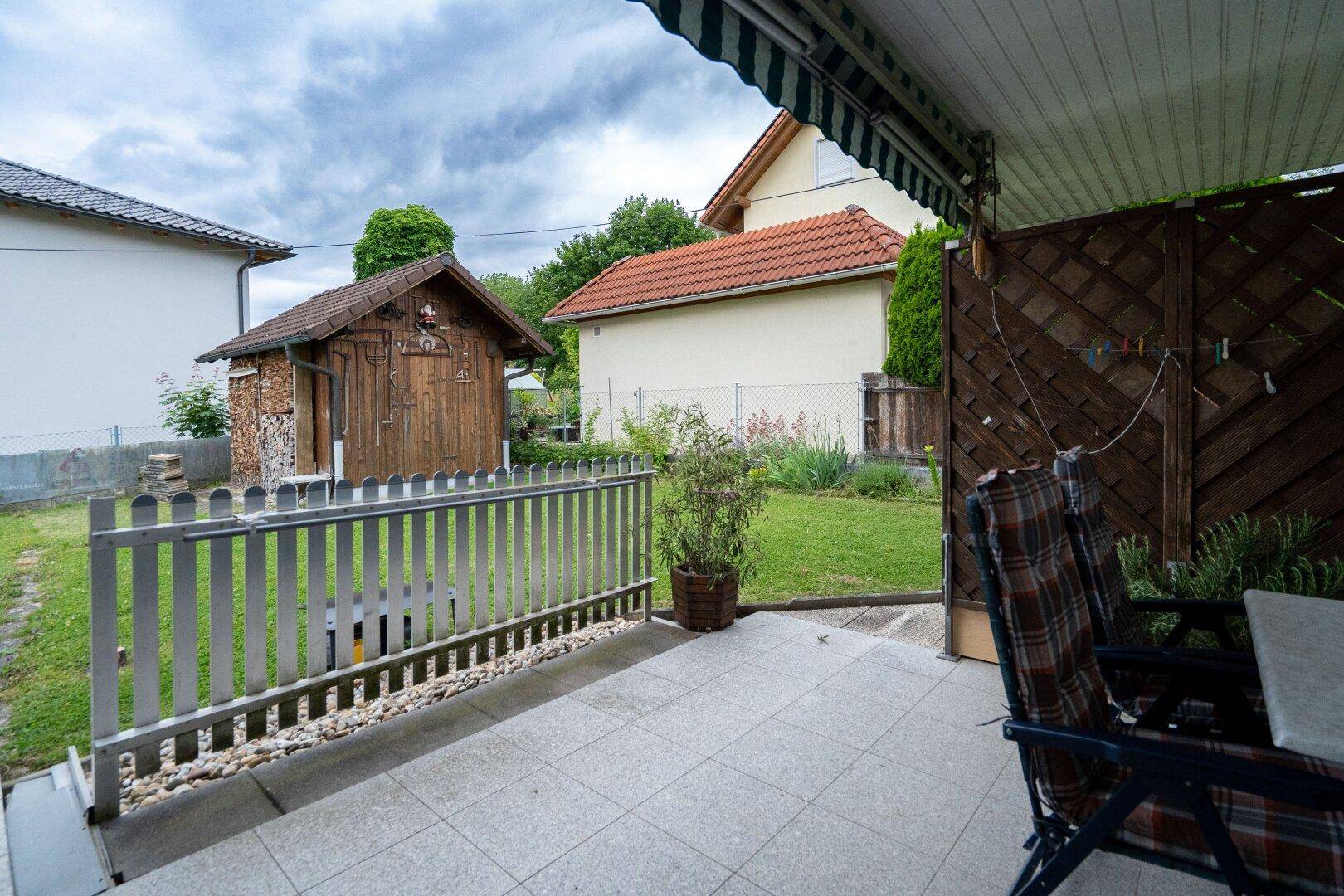 Überdachte Terrasse mit Fliesenboden und Blick auf den Garten mit Holzschuppen.