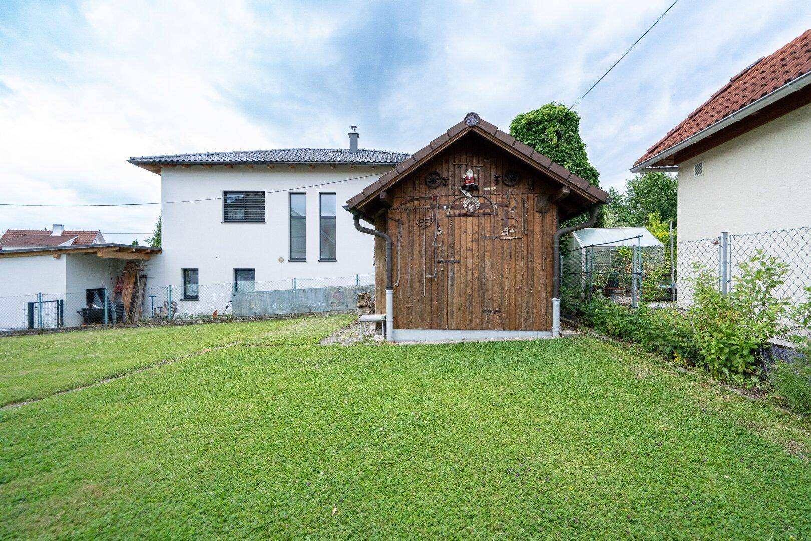 Großer, gepflegter Garten mit Rasenfläche, Holzschuppen und kleinem Gewächshaus.