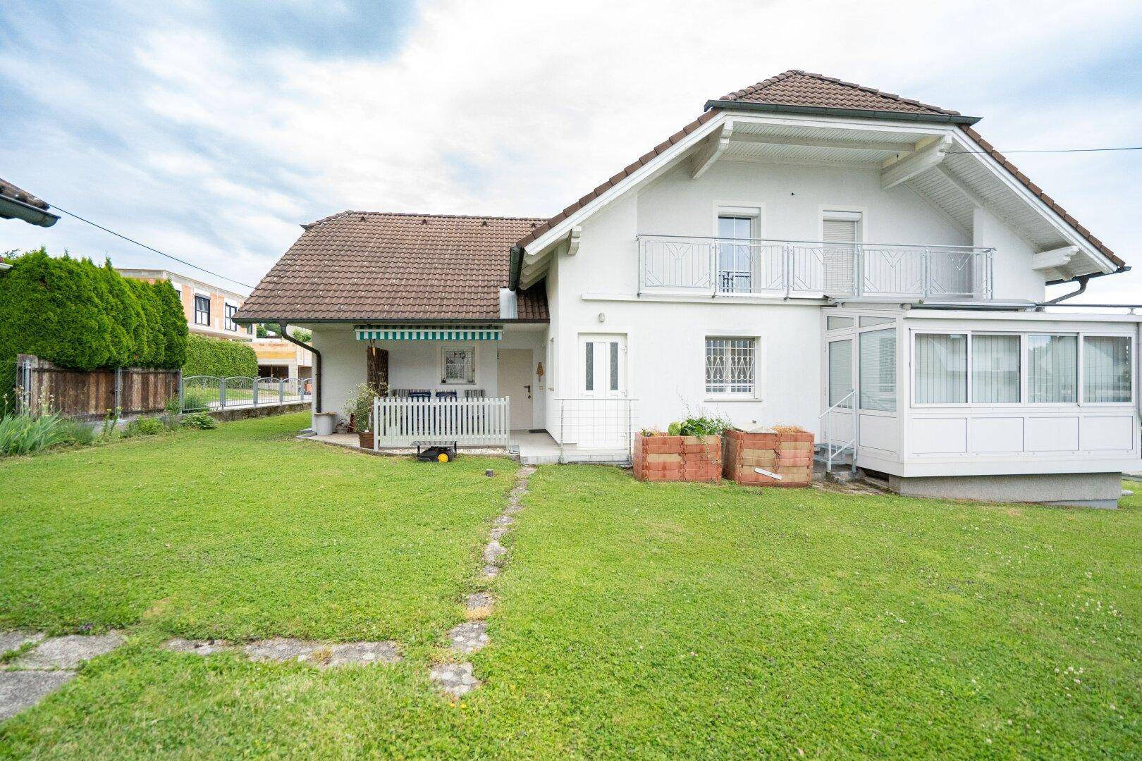 Rückansicht des Hauses mit weitläufigem Garten, Wintergarten und Zugang zur Terrasse.