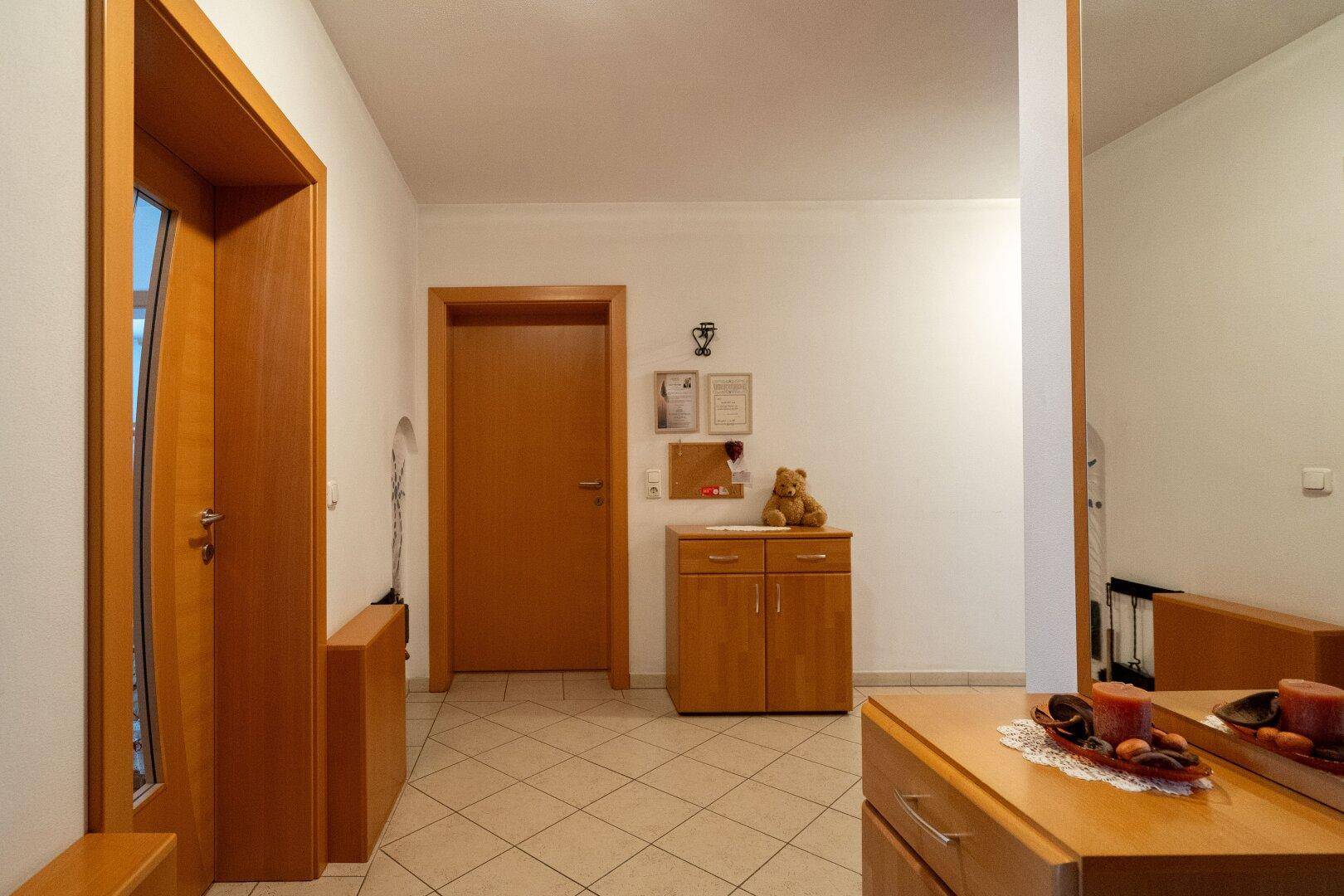 Heller Flur mit Fliesenboden, Holzmöbeln und einem großen Spiegel.