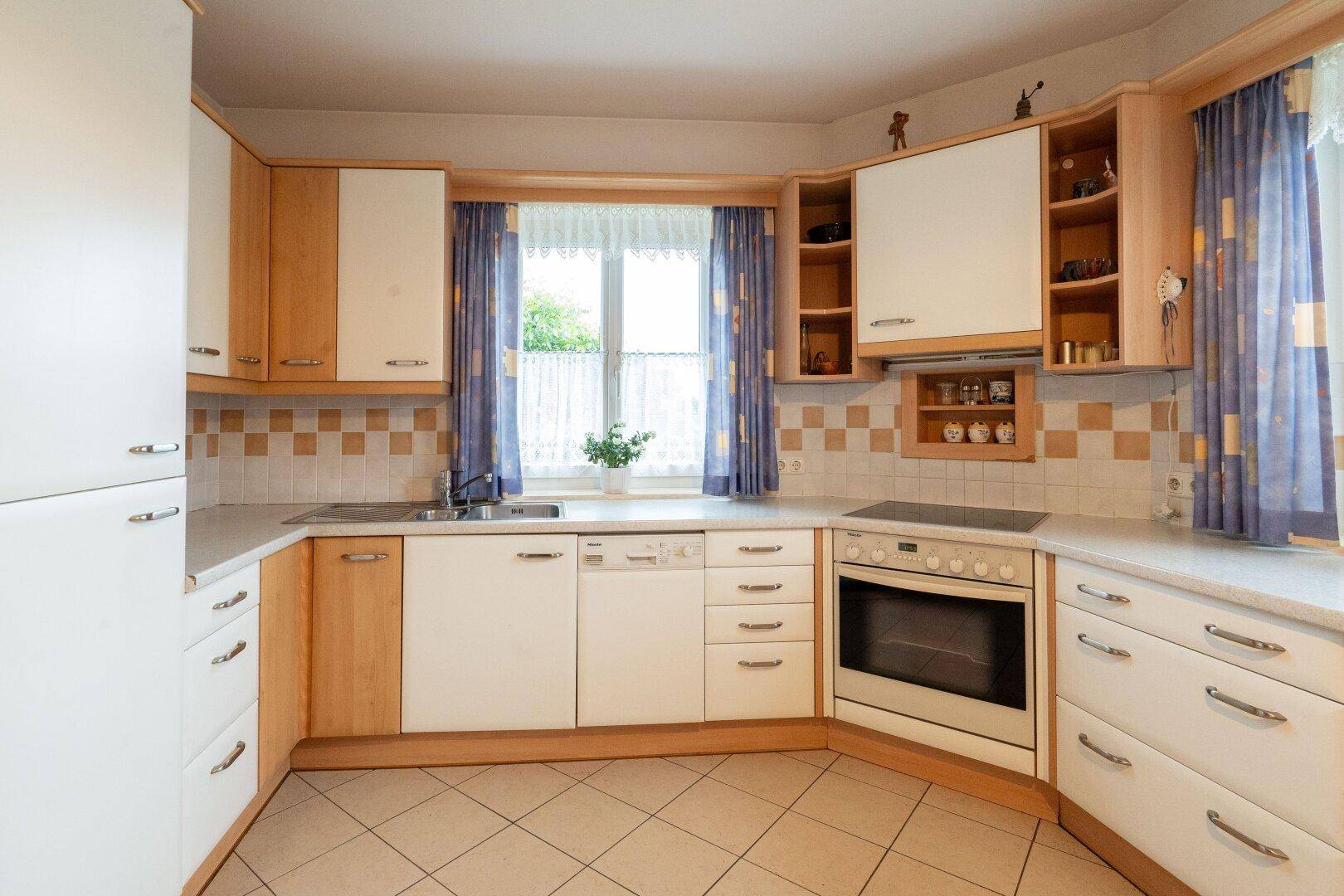 Funktionale Küche mit weißen und holzfarbenen Schränken, Spülmaschine und Herd.