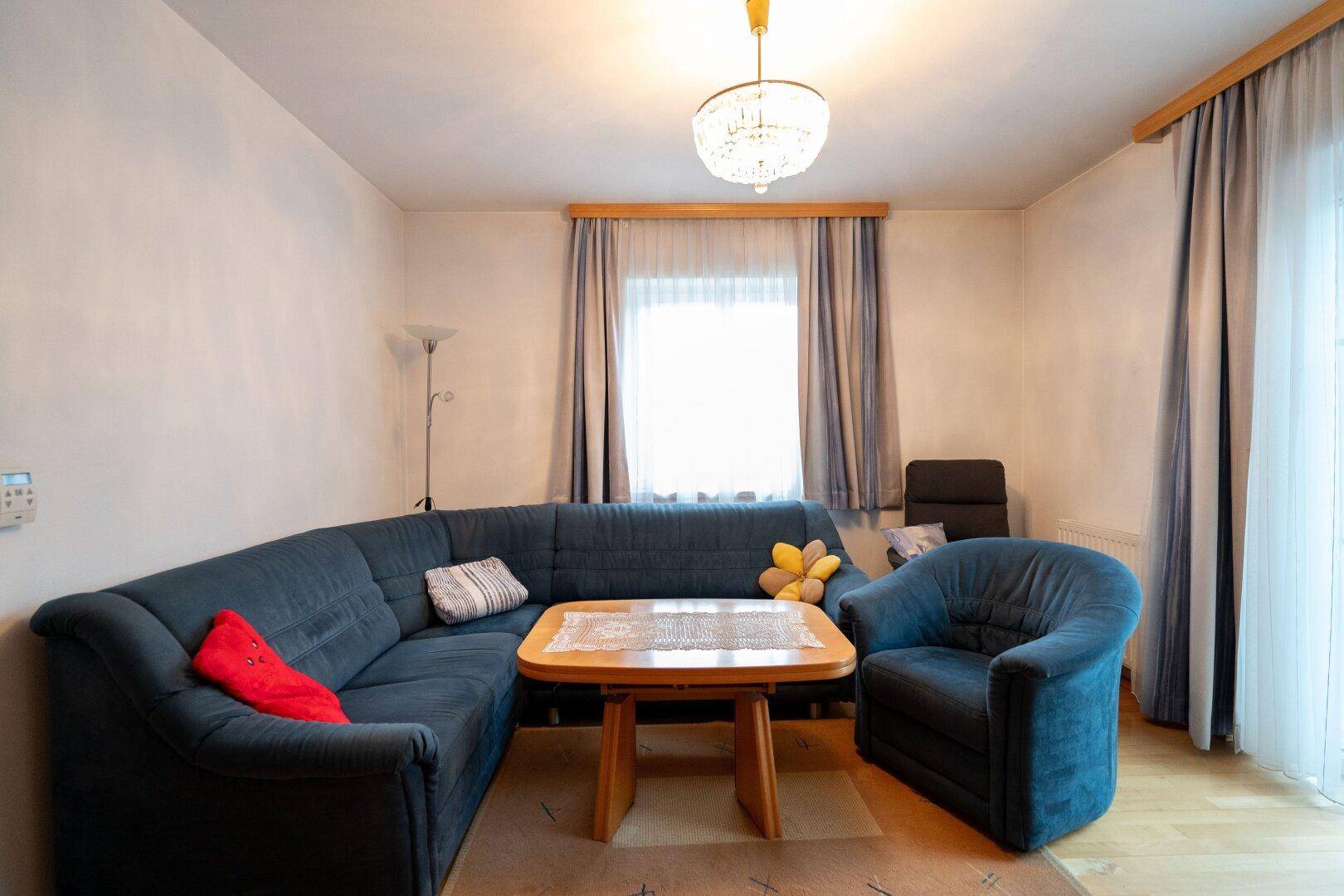 Gemütliches Wohnzimmer mit blauer Sofagarnitur, Holztisch und Zugang zum Balkon.