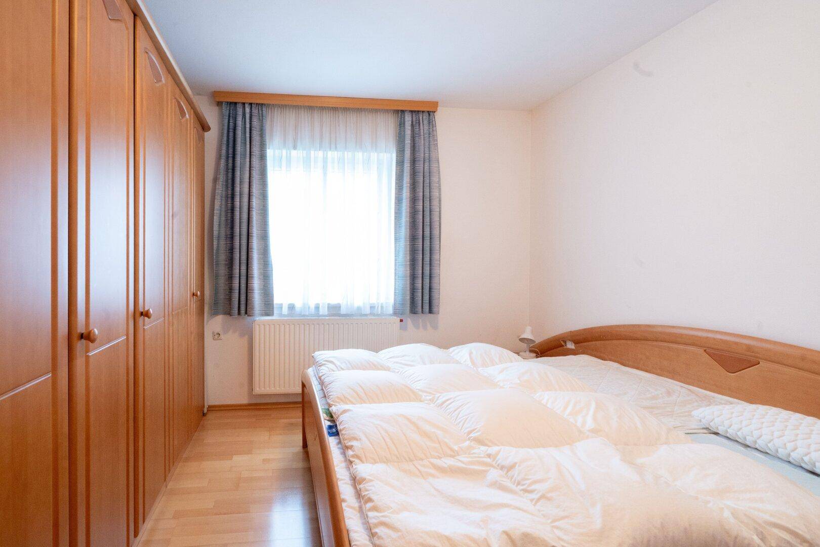 Schlafzimmer mit Holzbett, Einbauschränken und Fenster mit Blick ins Grüne.
