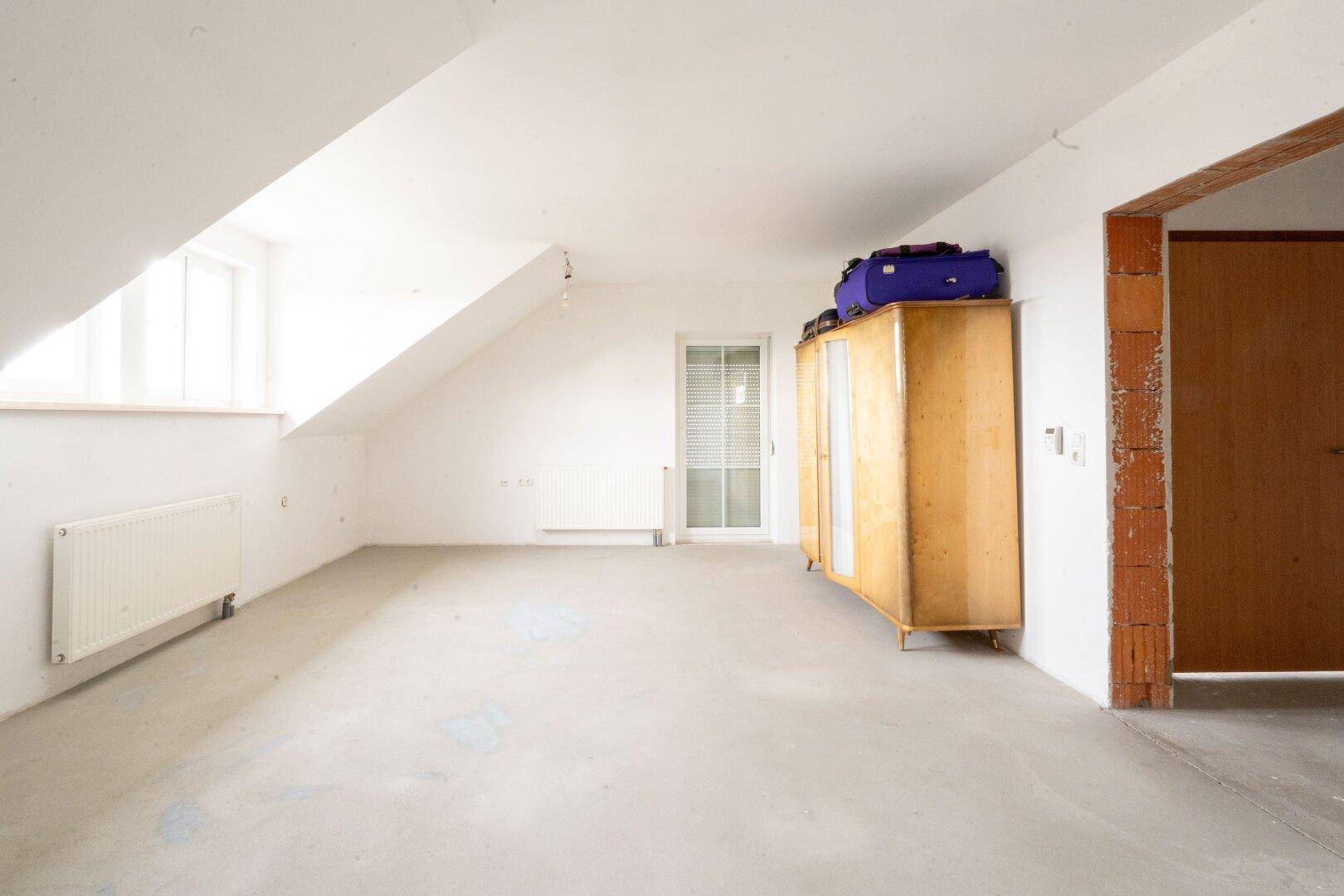 Heller Dachbodenraum mit schrägen Wänden, Fenster und Betonboden.