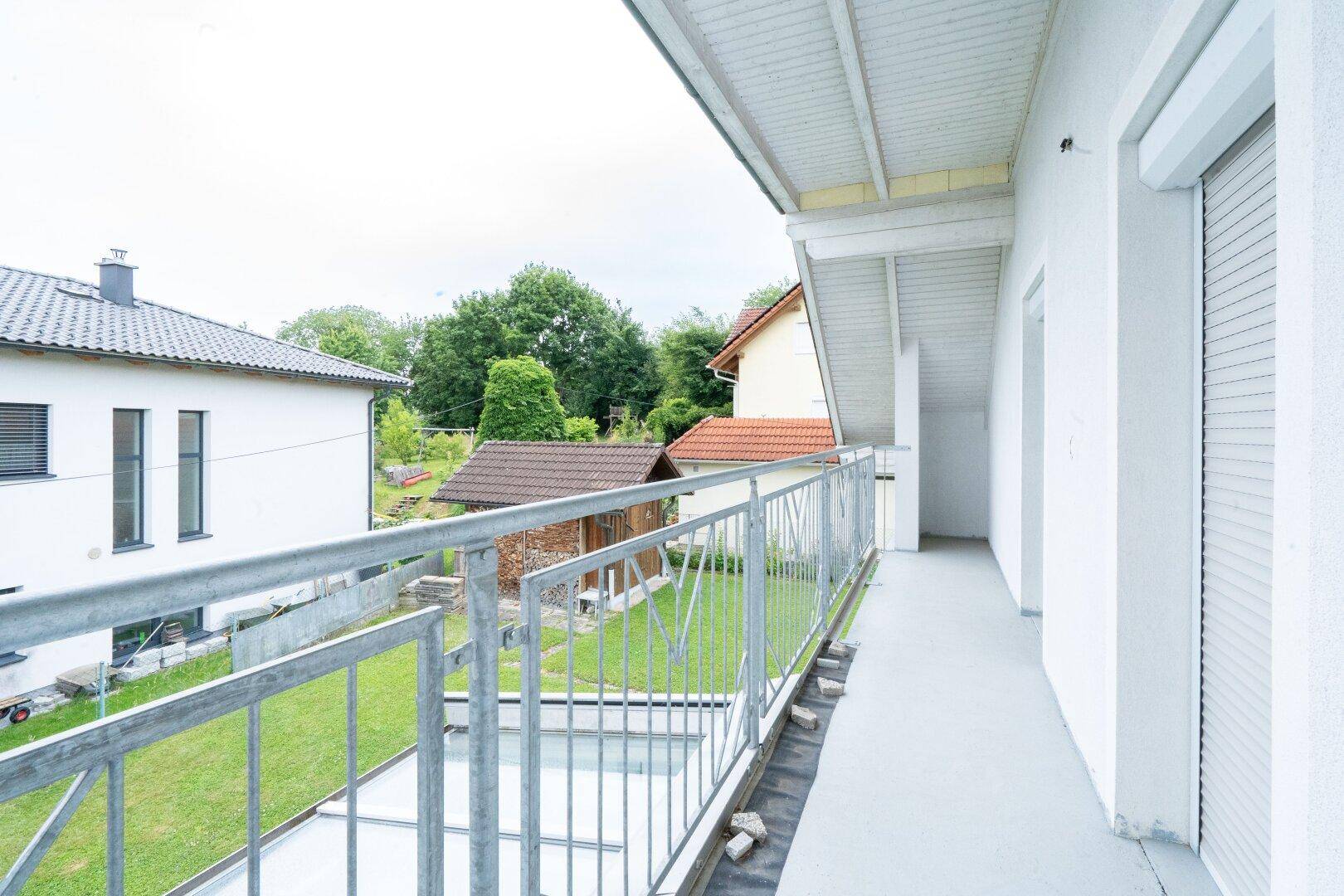 Langer Balkon mit Metallgeländer und Blick auf den Garten und die Umgebung.