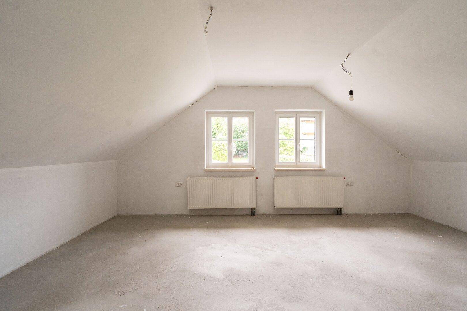 Großer Dachbodenraum im Rohbau mit zwei Fenstern und Betonboden.
