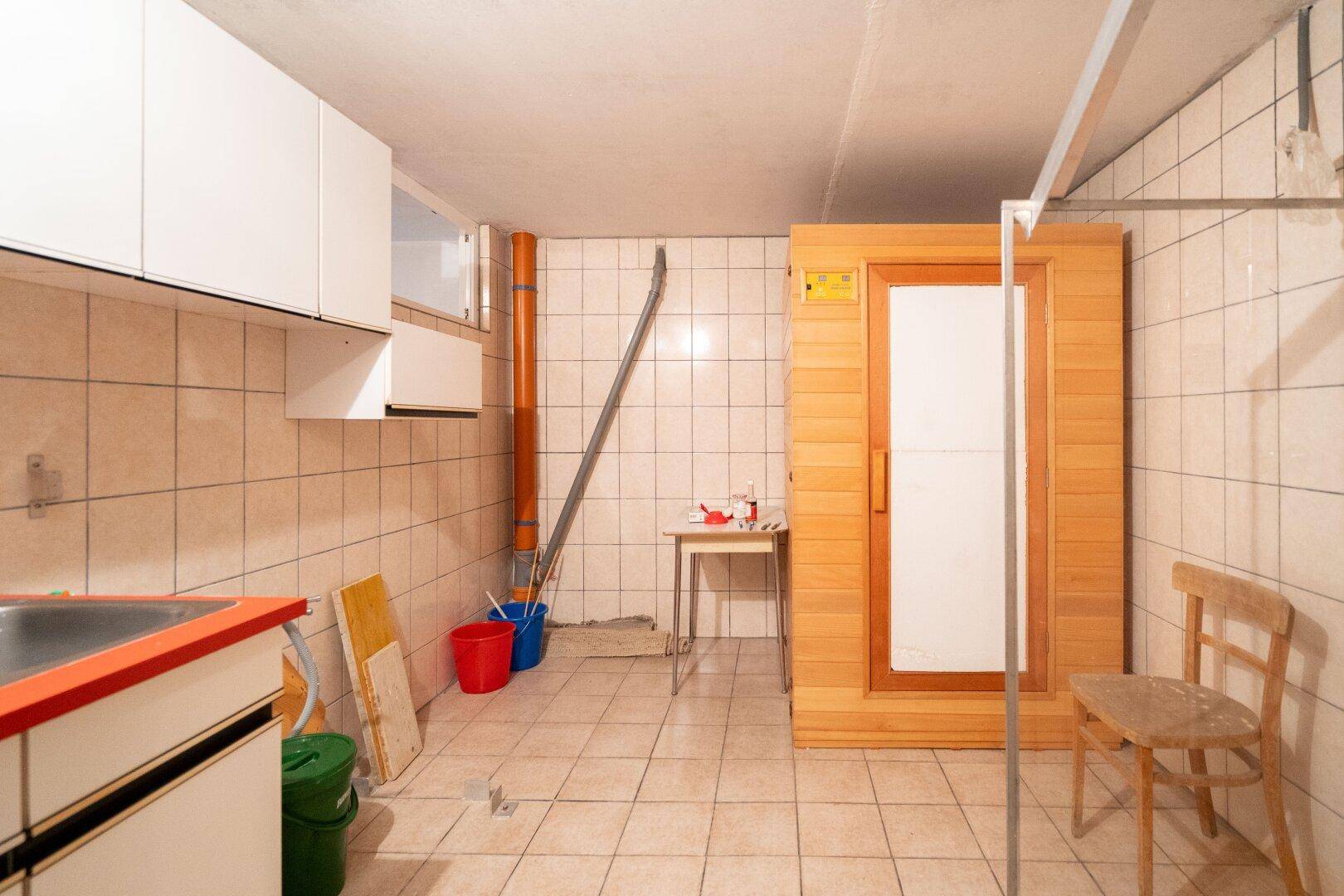 Kellerraum mit Fliesen, kleiner Spüle und einer eingebauten Sauna.
