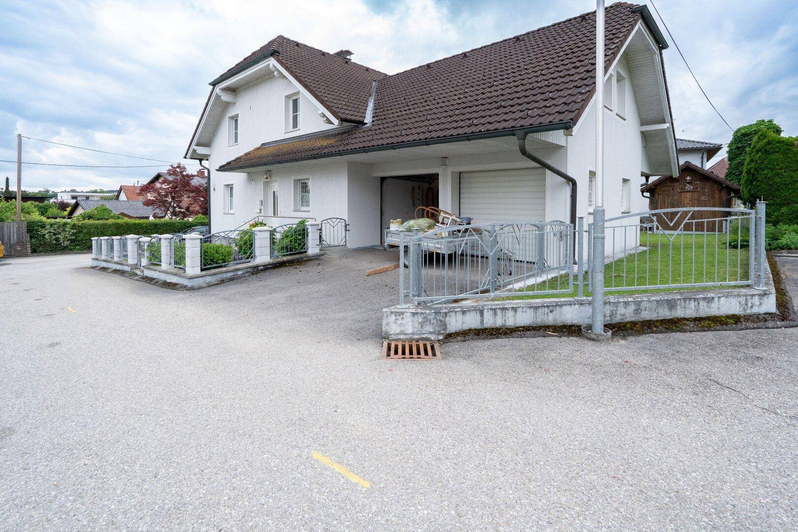 Weißes Einfamilienhaus mit braunem Dach, Garage und Zufahrt, inklusive Rampe.