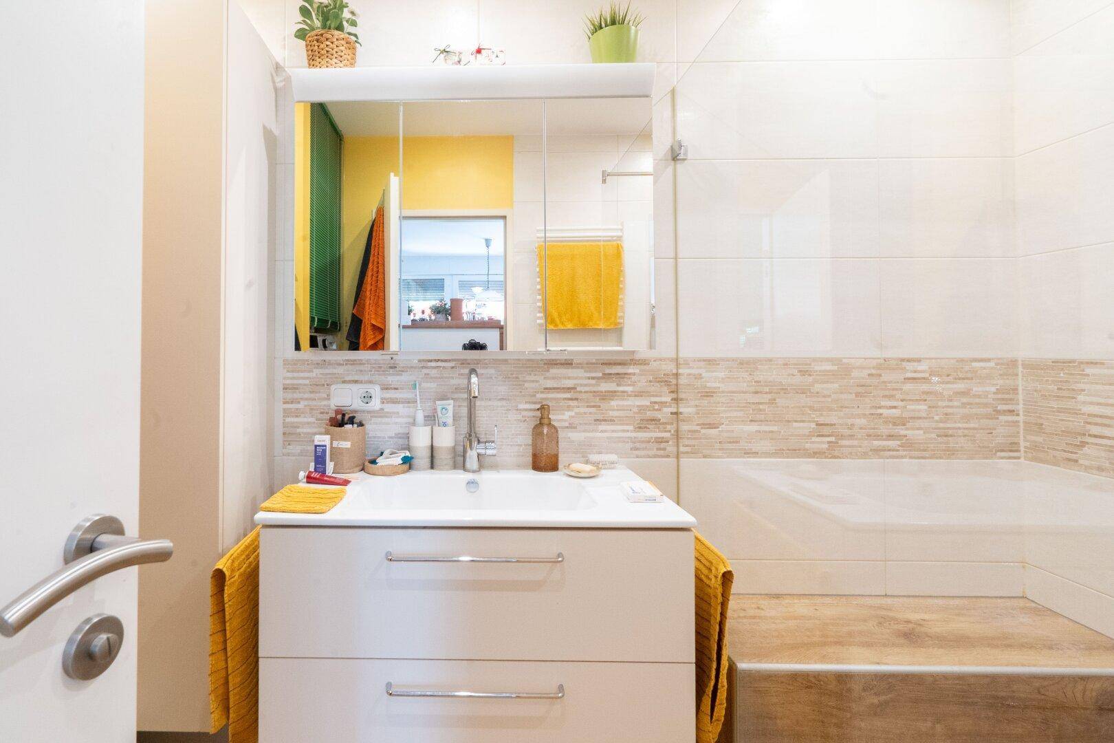 Helles Badezimmer mit modernem Waschtisch, Spiegel und begehbarer Dusche.