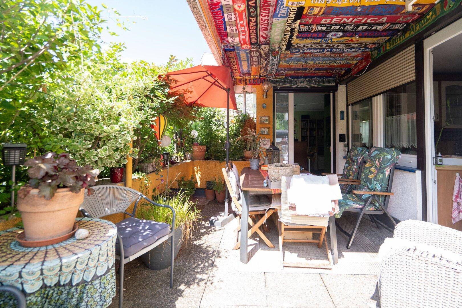 Bunte Terrasse mit Sitzgelegenheiten, Pflanzen und kreativer Deckenverkleidung.