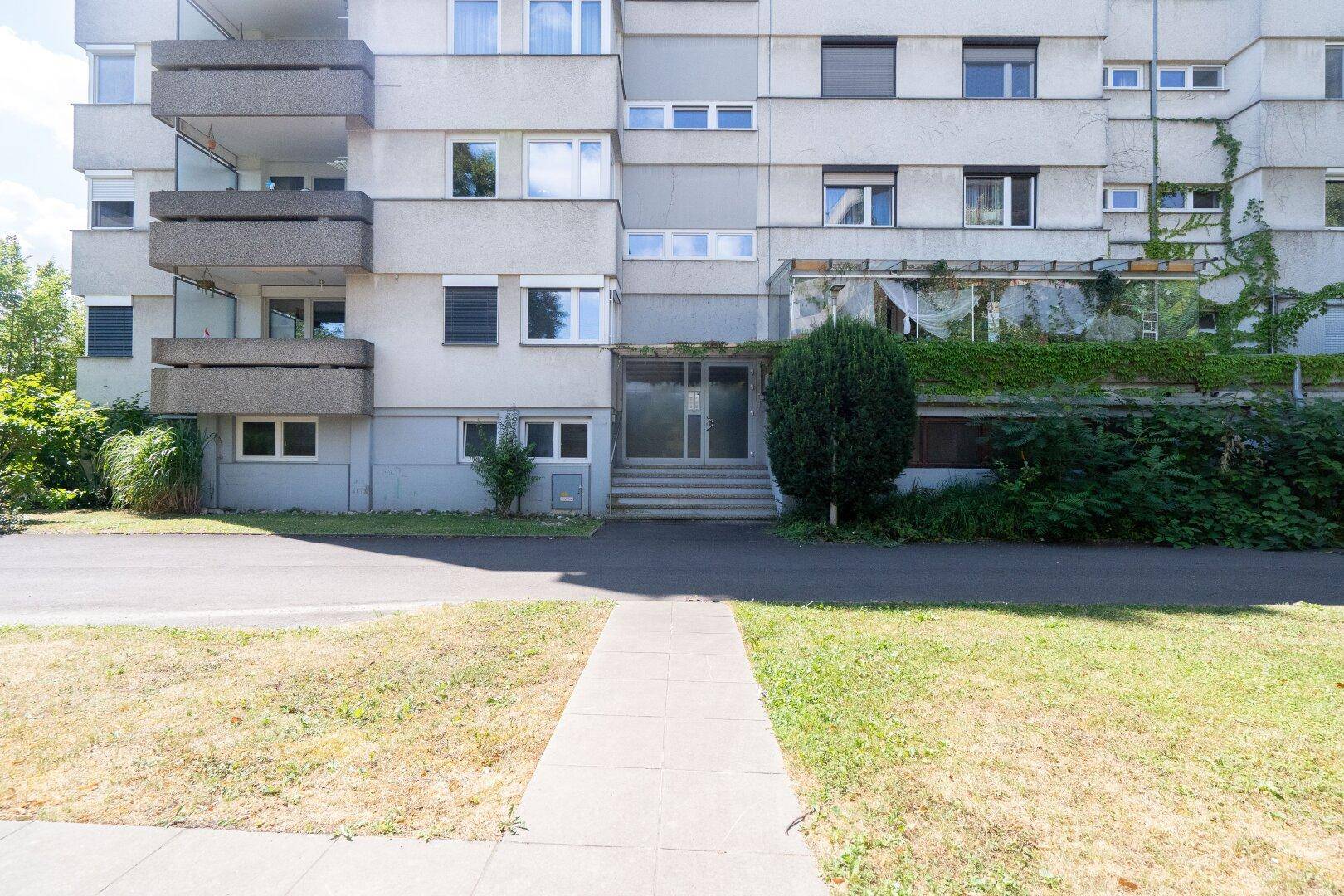 Eingangsbereich eines Mehrfamilienhauses mit gepflegtem Vorgarten und Gehwegen.