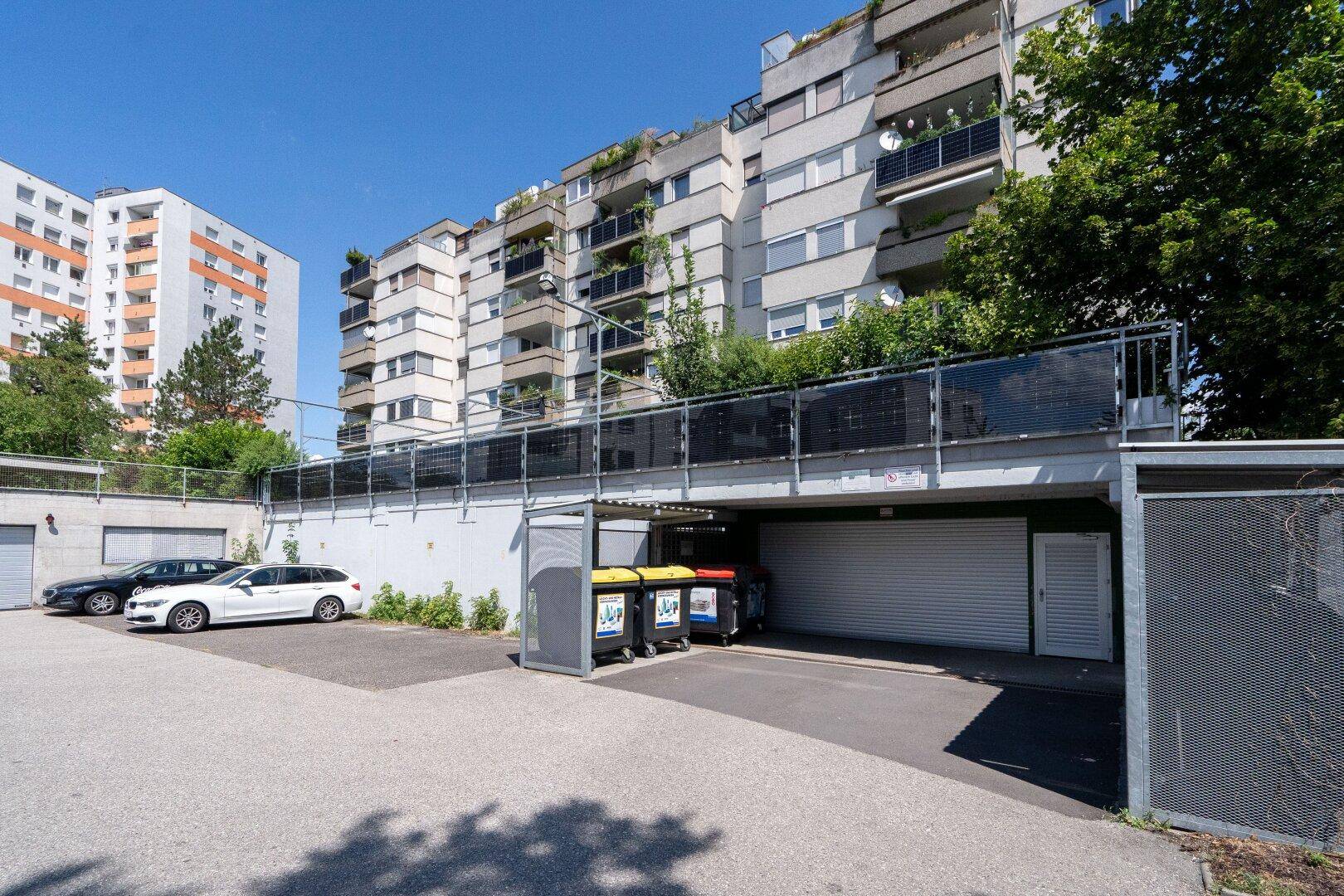 Außenansicht eines Wohnkomplexes mit Parkplätzen und Mülltonnenbereich.