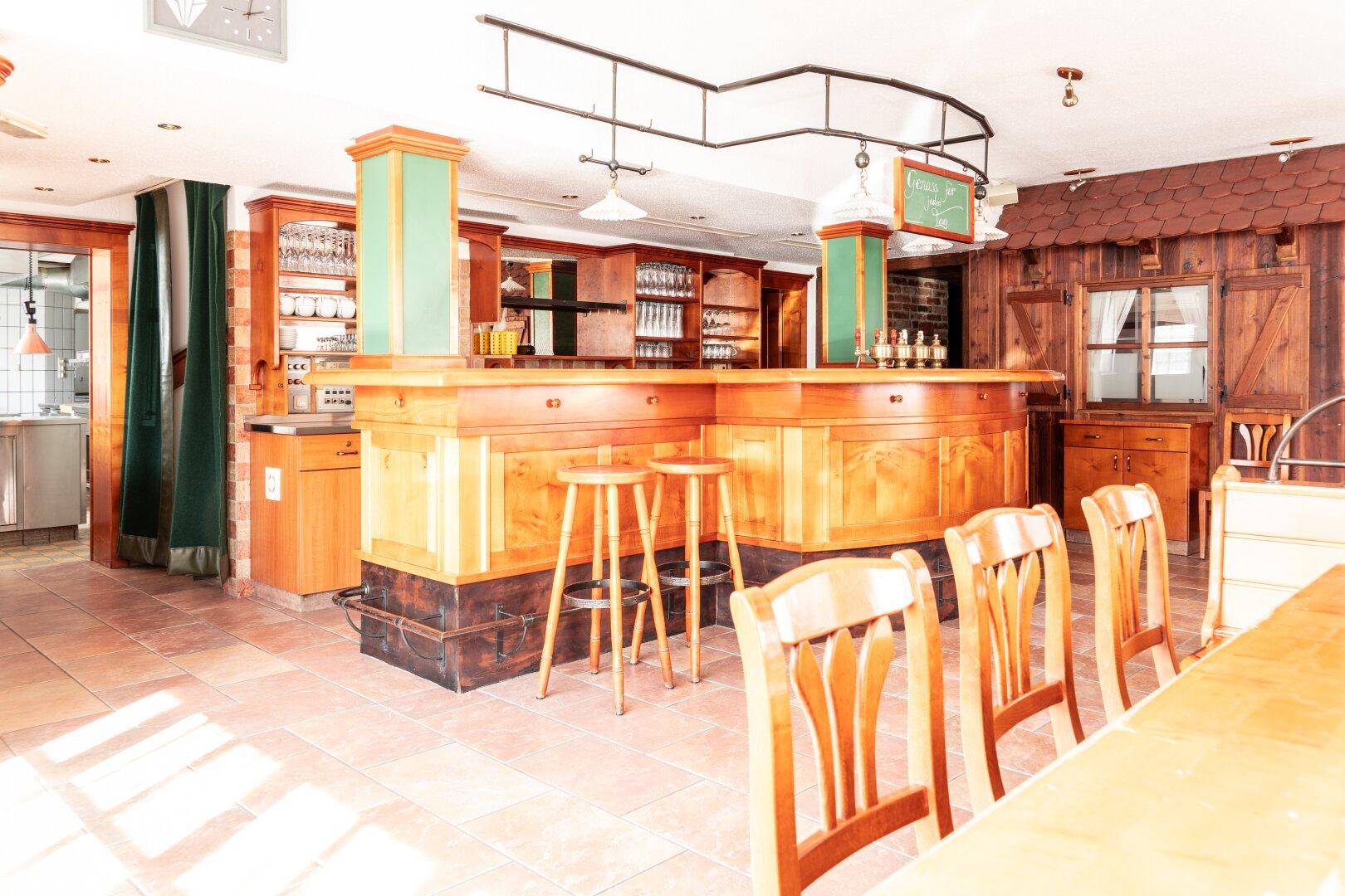 Gemütlicher Restaurantbereich mit einer großen Holzbar, Hockern und traditionellen Holzmöbeln.