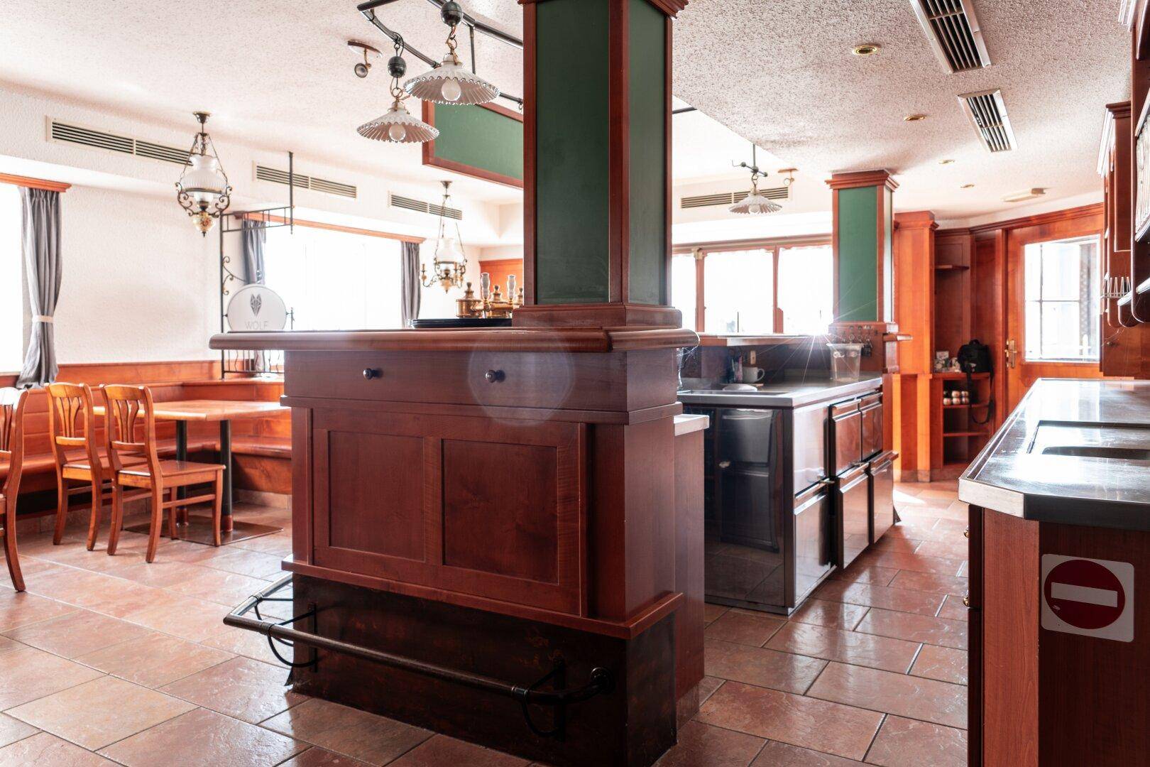 Bar- und Thekenbereich mit dunklen Holzmöbeln, Edelstahlflächen und traditionellen Deckenleuchten.