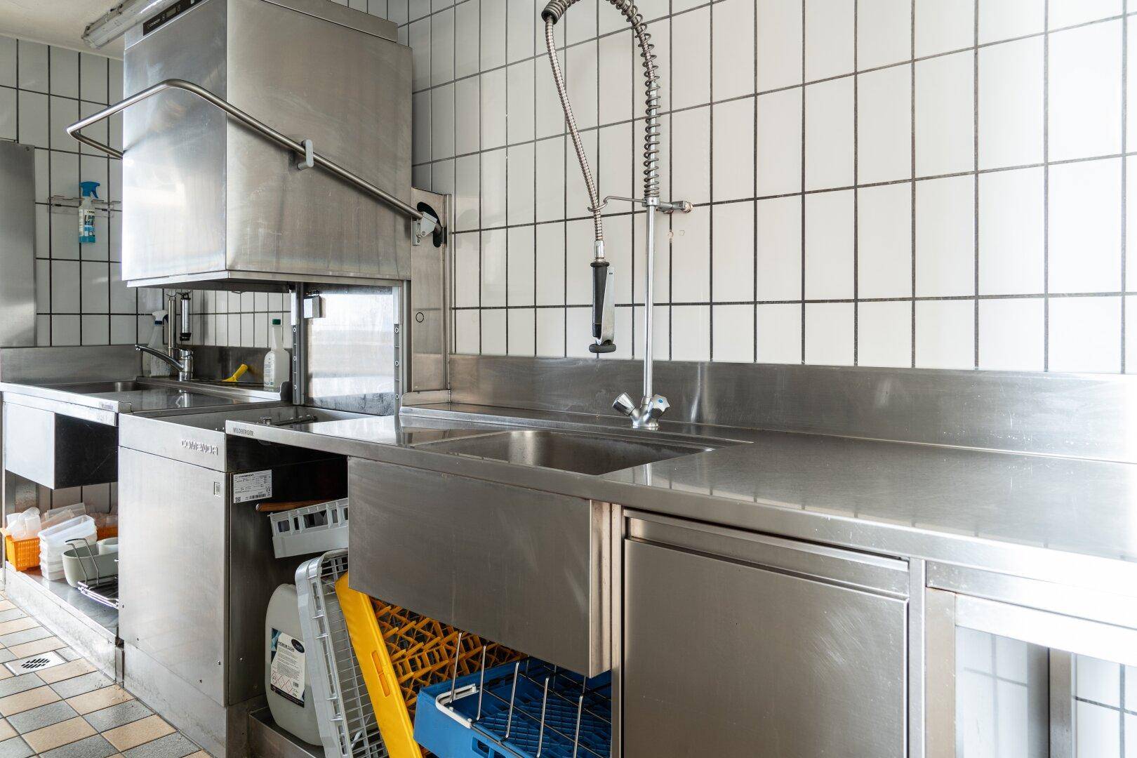 Professionelle Gastroküche mit Edelstahlgeräten, Spülbecken und gefliesten Wänden für effizienten Betrieb.