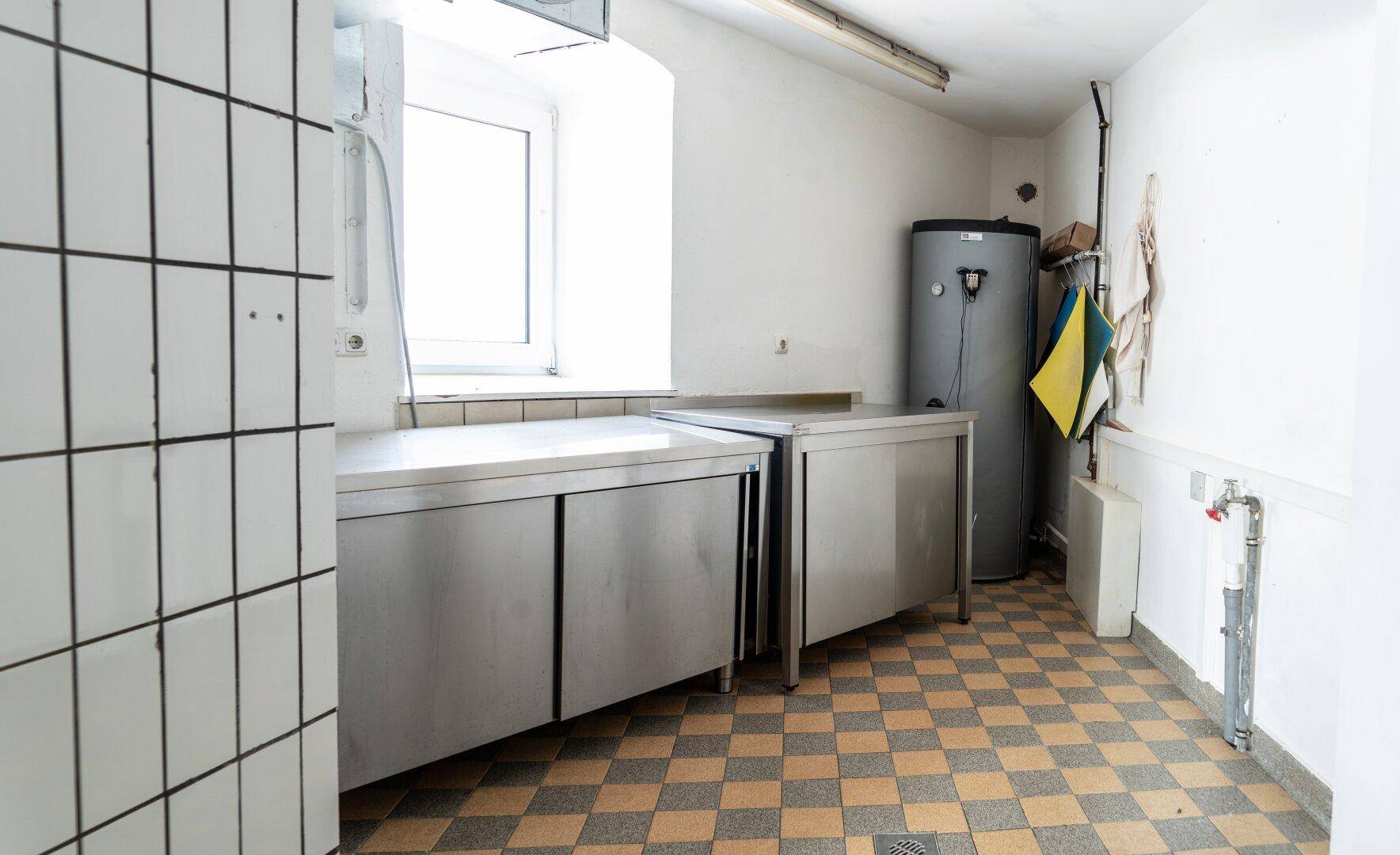 Praktischer Wirtschaftsraum mit Edelstahl-Arbeitsflächen, Fenster und einem Warmwasserspeicher.