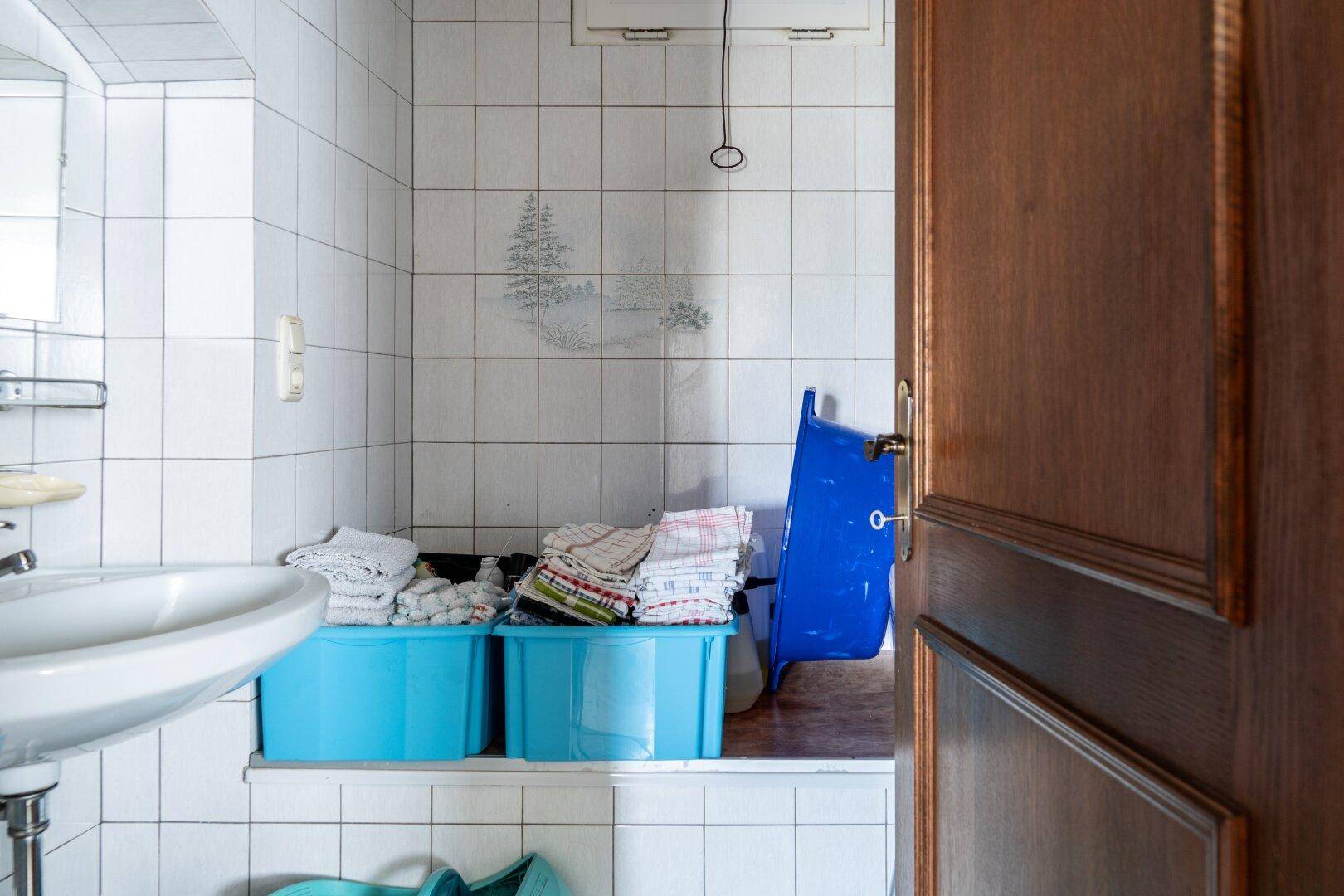 Badezimmer oder Waschraum mit weißen Fliesen, Waschbecken und blauen Aufbewahrungsboxen.