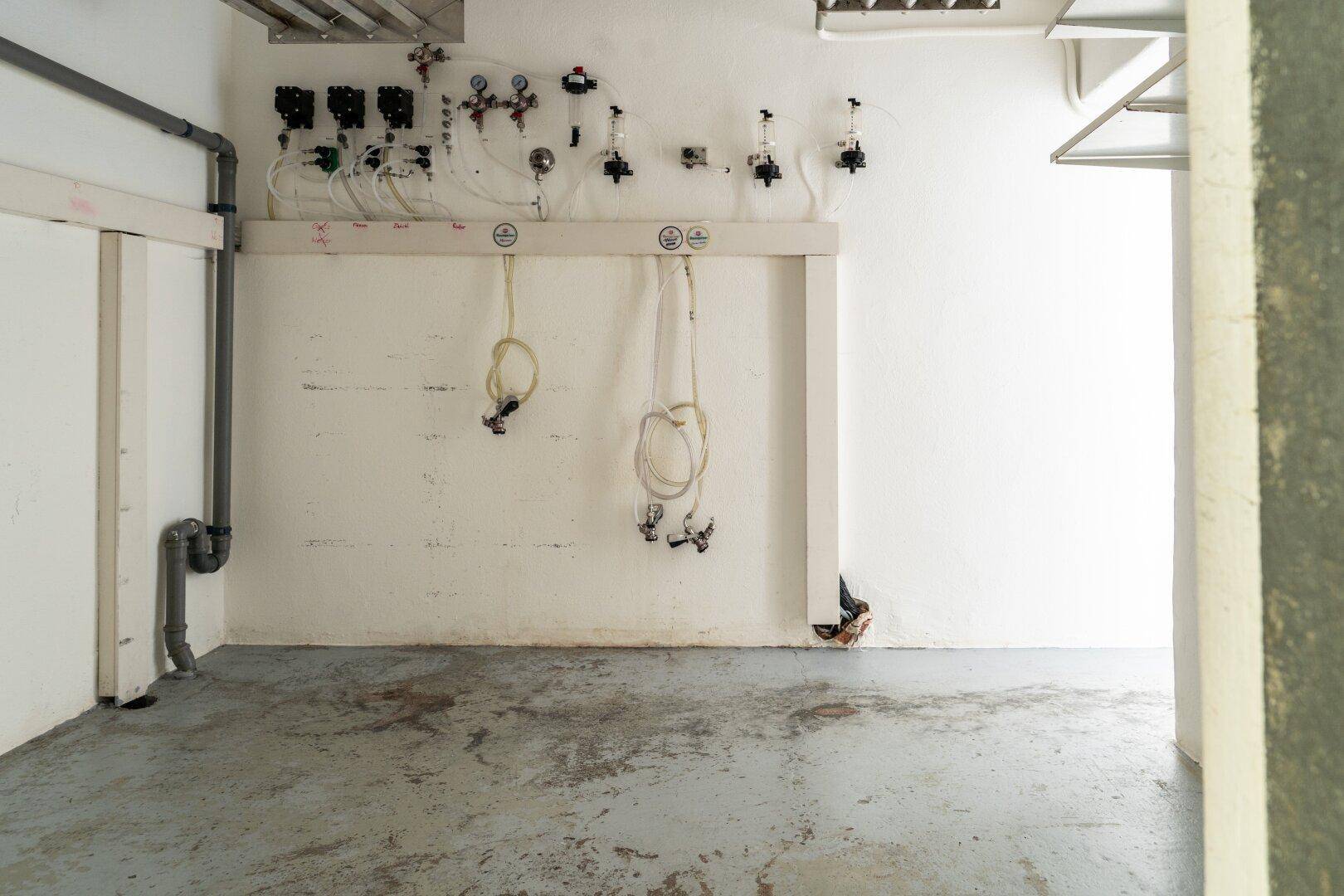 Kellerraum mit weißen Wänden, Betonboden und einem Zapfanlagensystem an der Wand.