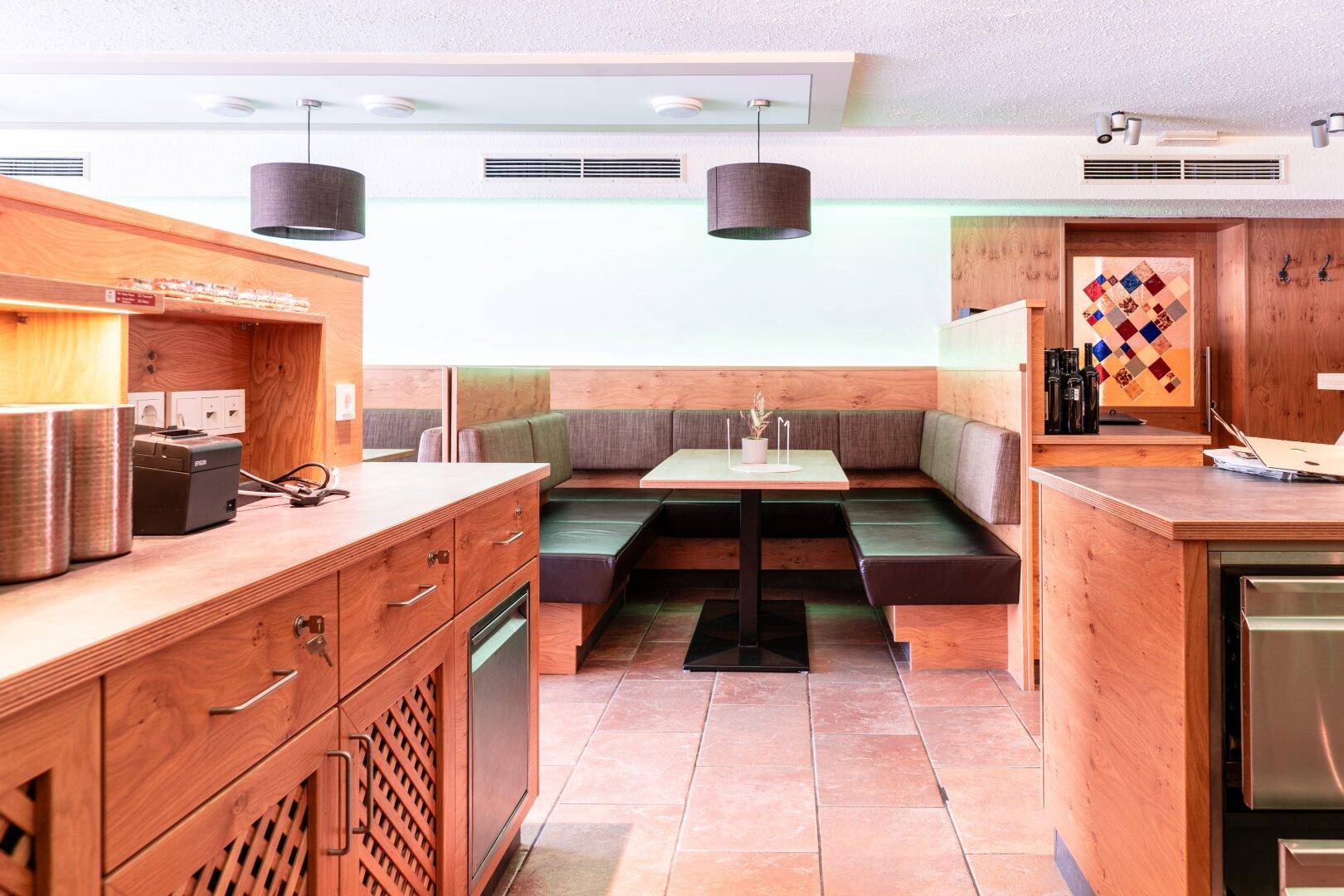 Gemütlicher Restaurantbereich mit Holzbänken, Tischen und moderner Beleuchtung, ideal für Gäste.