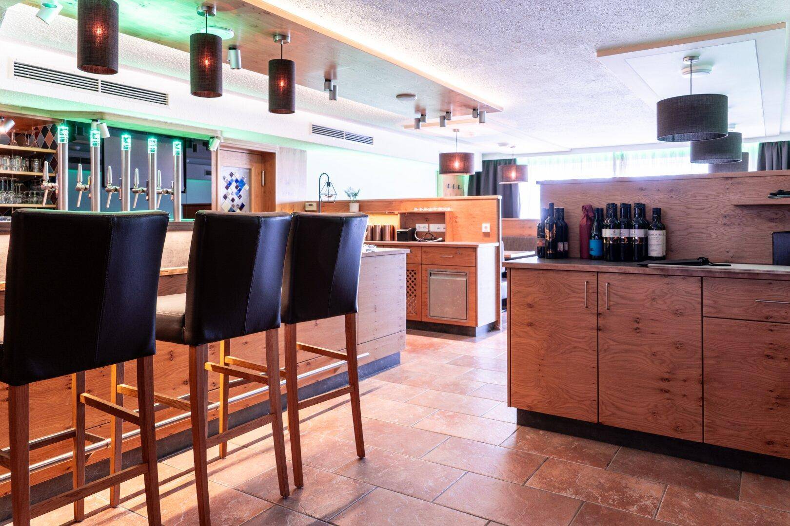 Moderne Bar mit Holztheke, Barhockern und Fliesenboden, beleuchtet mit farbigen Lichtern.