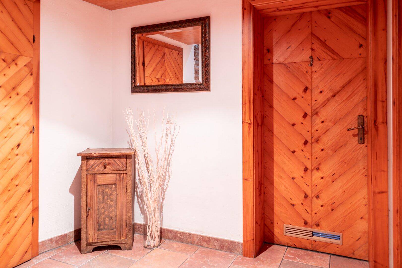 Eingangsbereich oder Flur mit Holztür, kleinem Holzschrank, Spiegel und Terrakottafliesenboden.