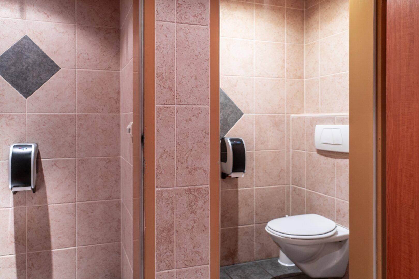 Öffentliche Toilette mit Toilettenkabinen, gefliesten Wänden und wandhängenden Toiletten.