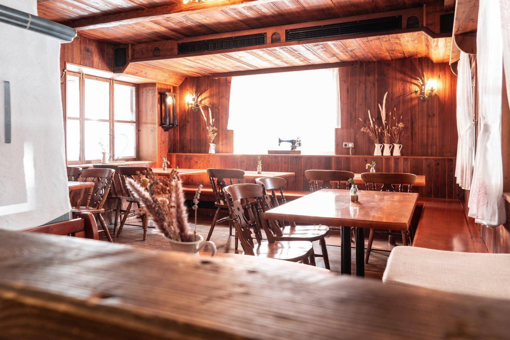 Warmer Gastraum mit Holzwänden, Holzboden und traditionellen Holzmöbeln, beleuchtet durch Fenster.