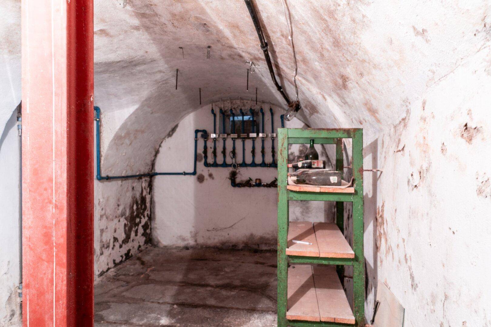 Weiterer Blick in den alten Keller mit Gewölbedecke, sichtbaren Rohren und einem kleinen Fenster.