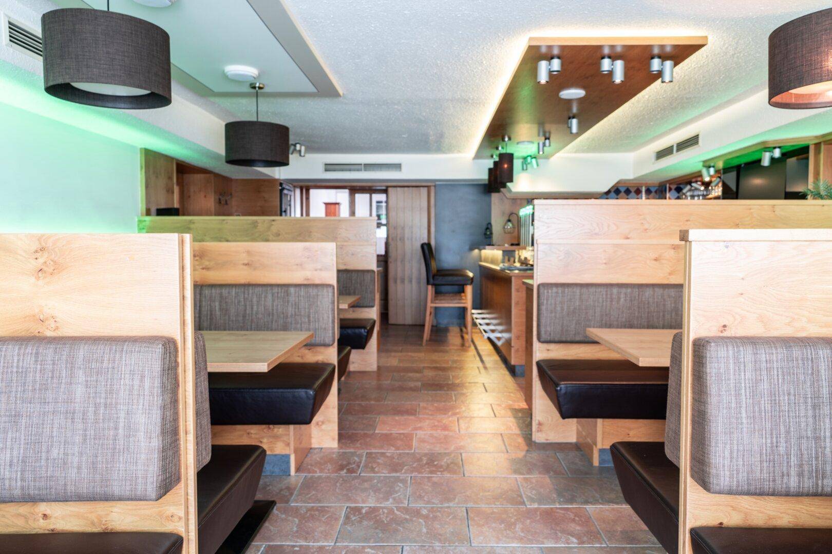 Restaurantbereich mit Holzbänken, Tischen und moderner Beleuchtung, der eine einladende Atmosphäre bietet.