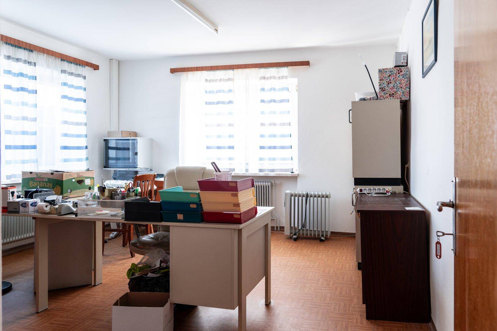 Funktionales Büro mit Schreibtisch, Stühlen und Fenstern, ausgestattet für den täglichen Arbeitsgebrauch.