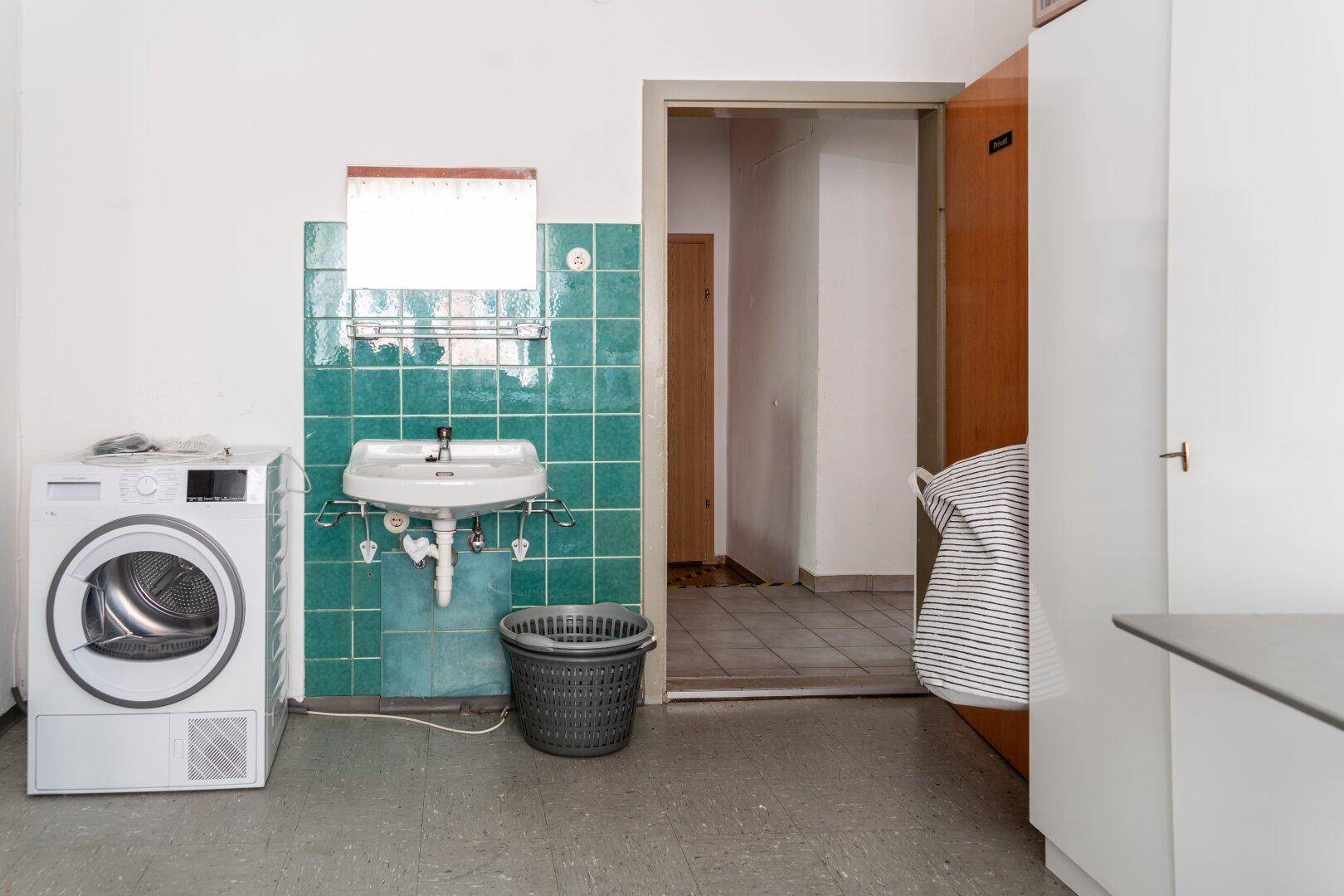 Waschküche mit Waschmaschine, Trockner und Waschbecken, ausgestattet mit grünen Fliesen an der Wand.