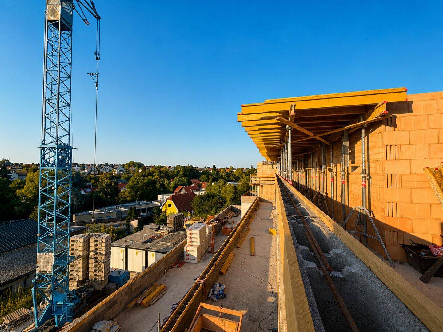 Blick von der Baustelle eines Neubaus auf die umliegende Wohnsiedlung und den Baukran.