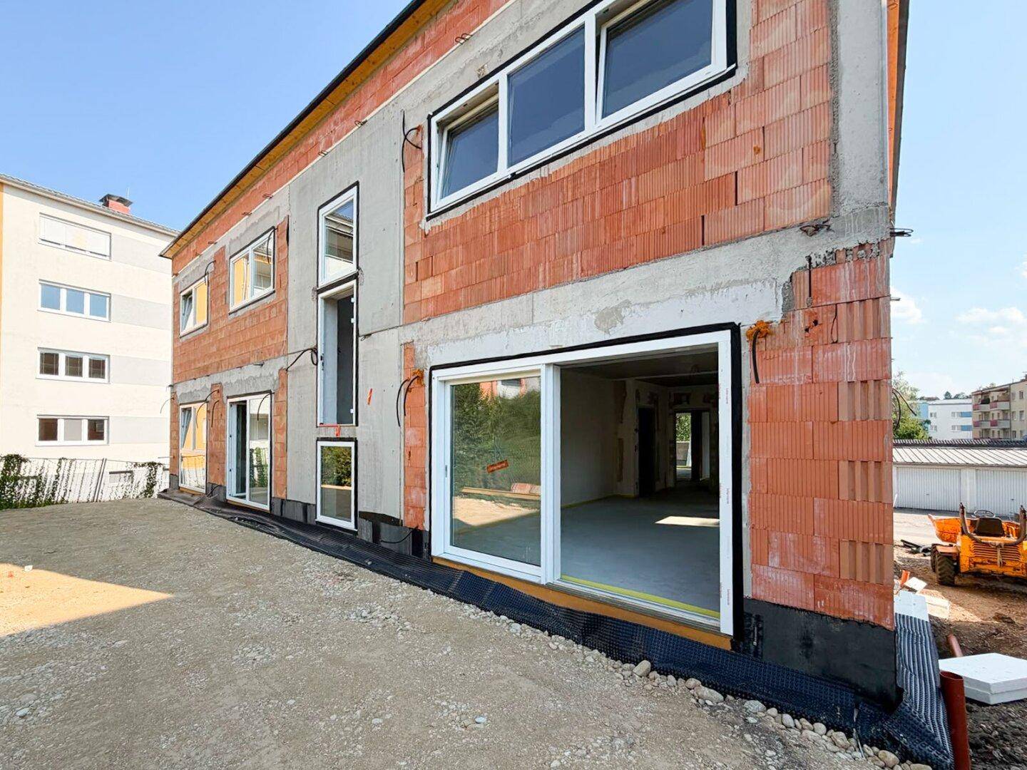 Seitenansicht des Neubaus im Rohbau mit großen Fensteröffnungen und Schiebetüren.