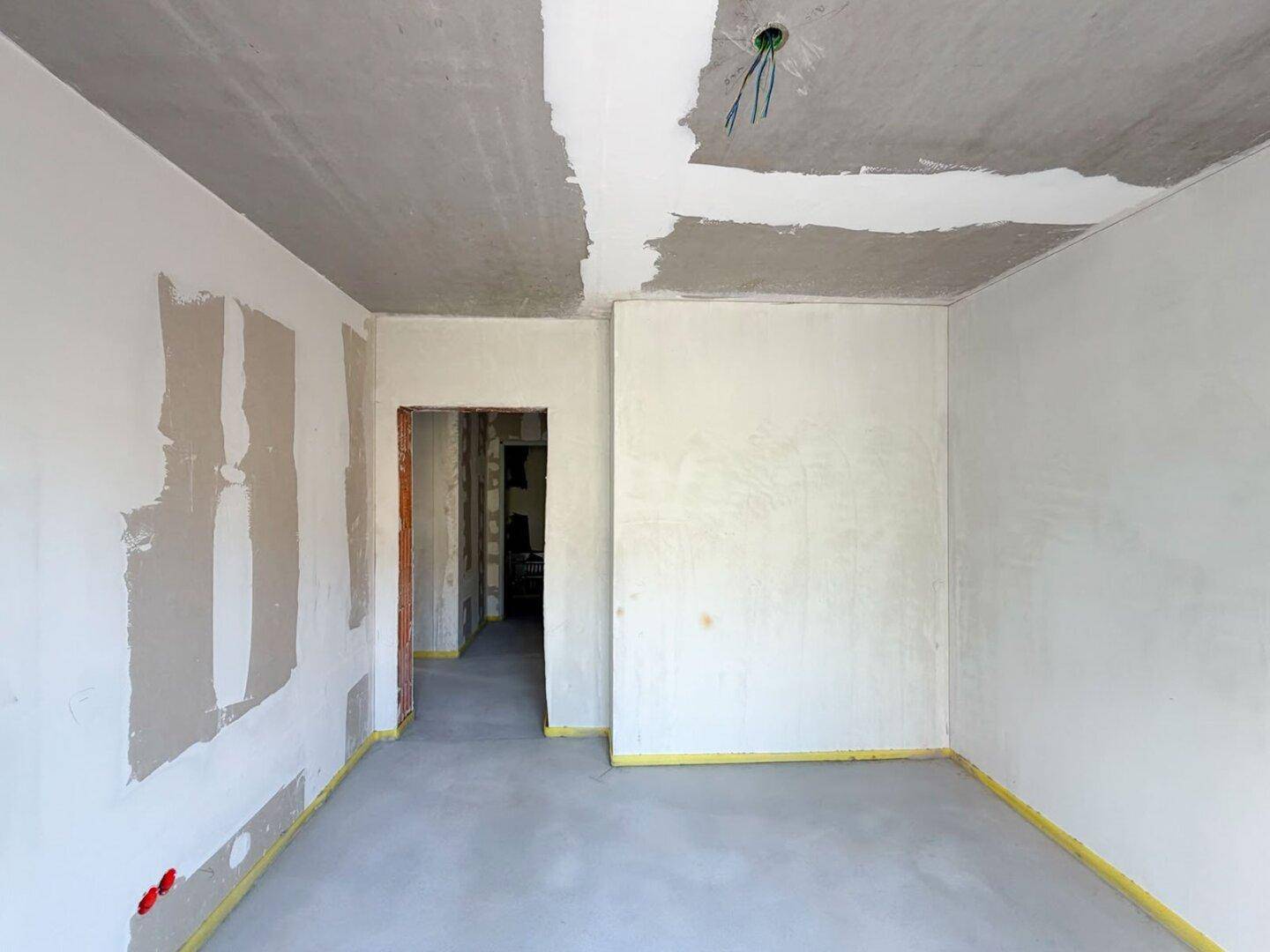 Unfertiger Innenraum im Rohbau mit teilweise verputzten Wänden und Betonboden.